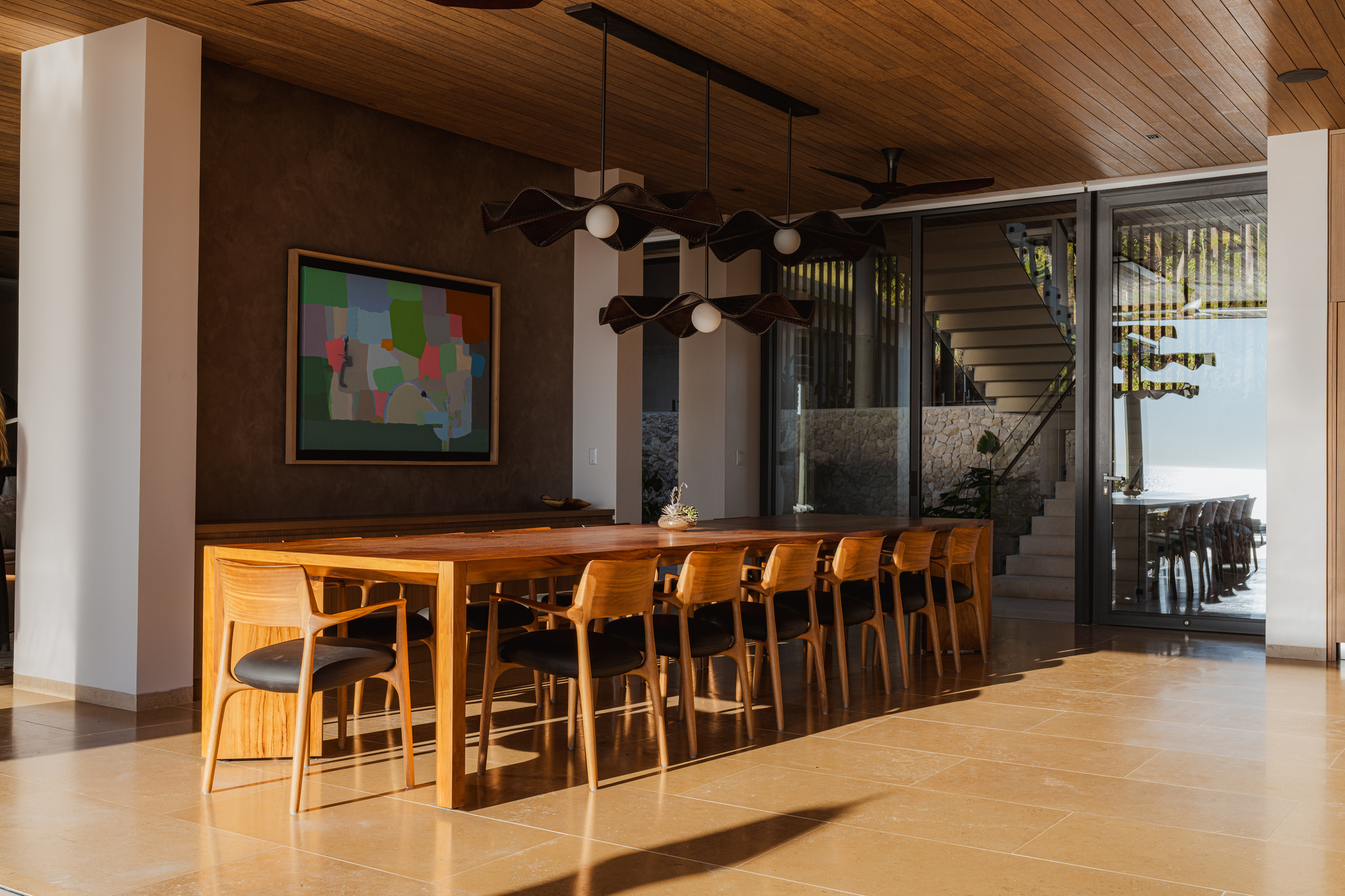 Dining area with timber table and pendant lights beneath wood slat ceiling looking toward exterior stairs