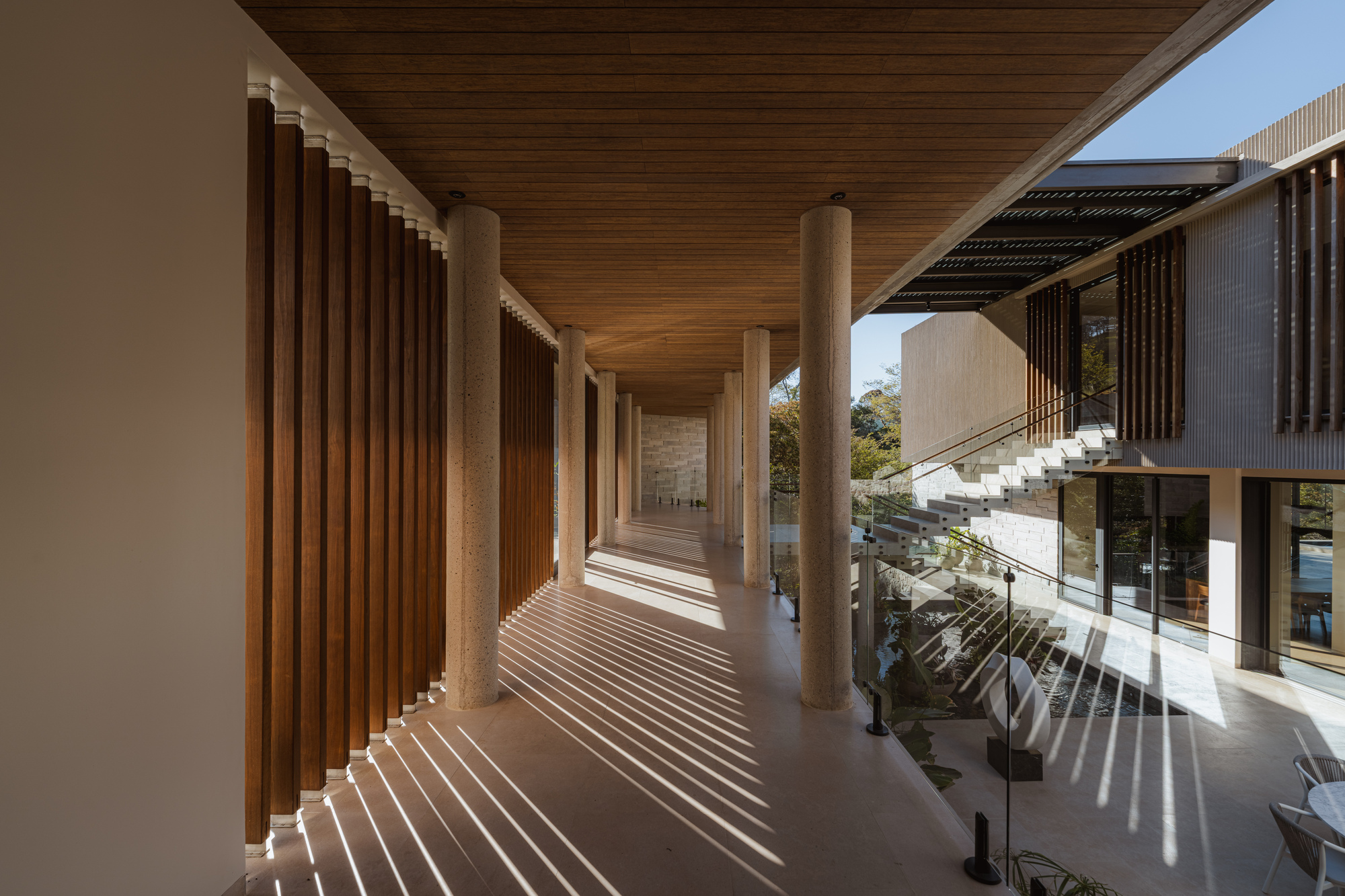 Covered walkway with concrete columns and timber ceiling casting striped shadows across the floor