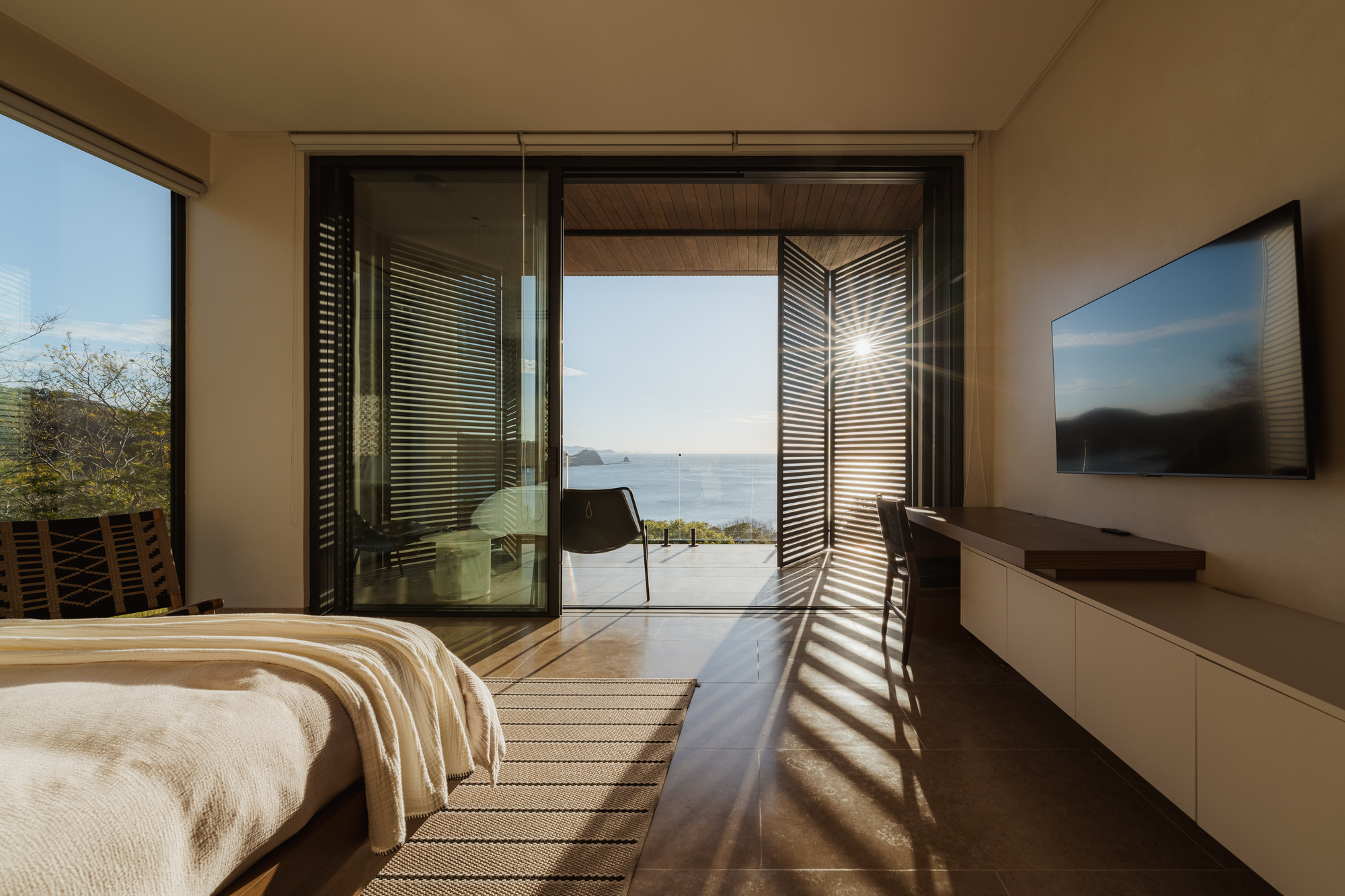 Bedroom with open sliding doors framing an ocean view and casting louvered sunlight patterns