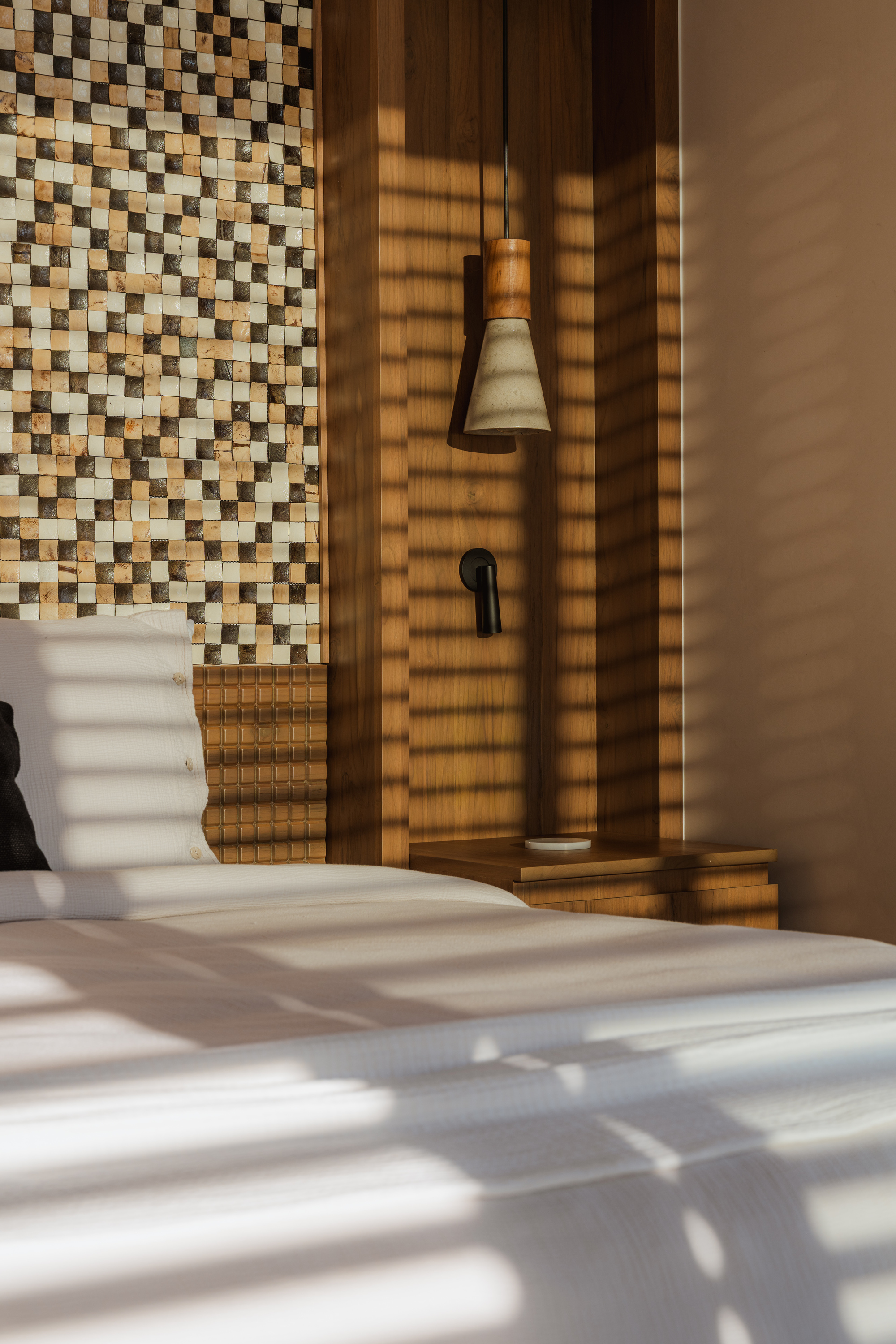 Mosaic tile wall beside timber slat partition with pendant light and afternoon shadow play