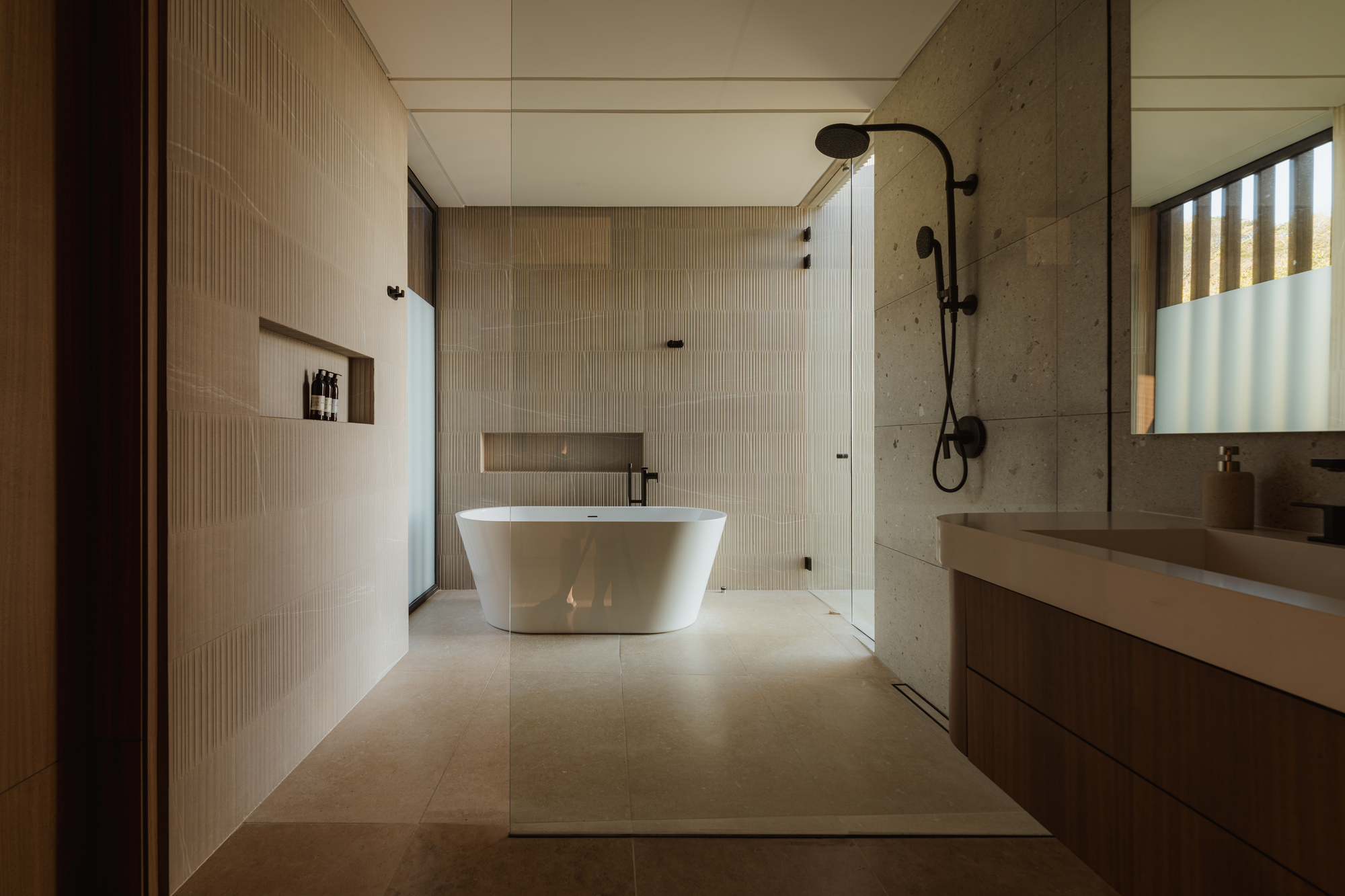 Bathroom with freestanding tub, glass shower screen, concrete wall and horizontal window openings