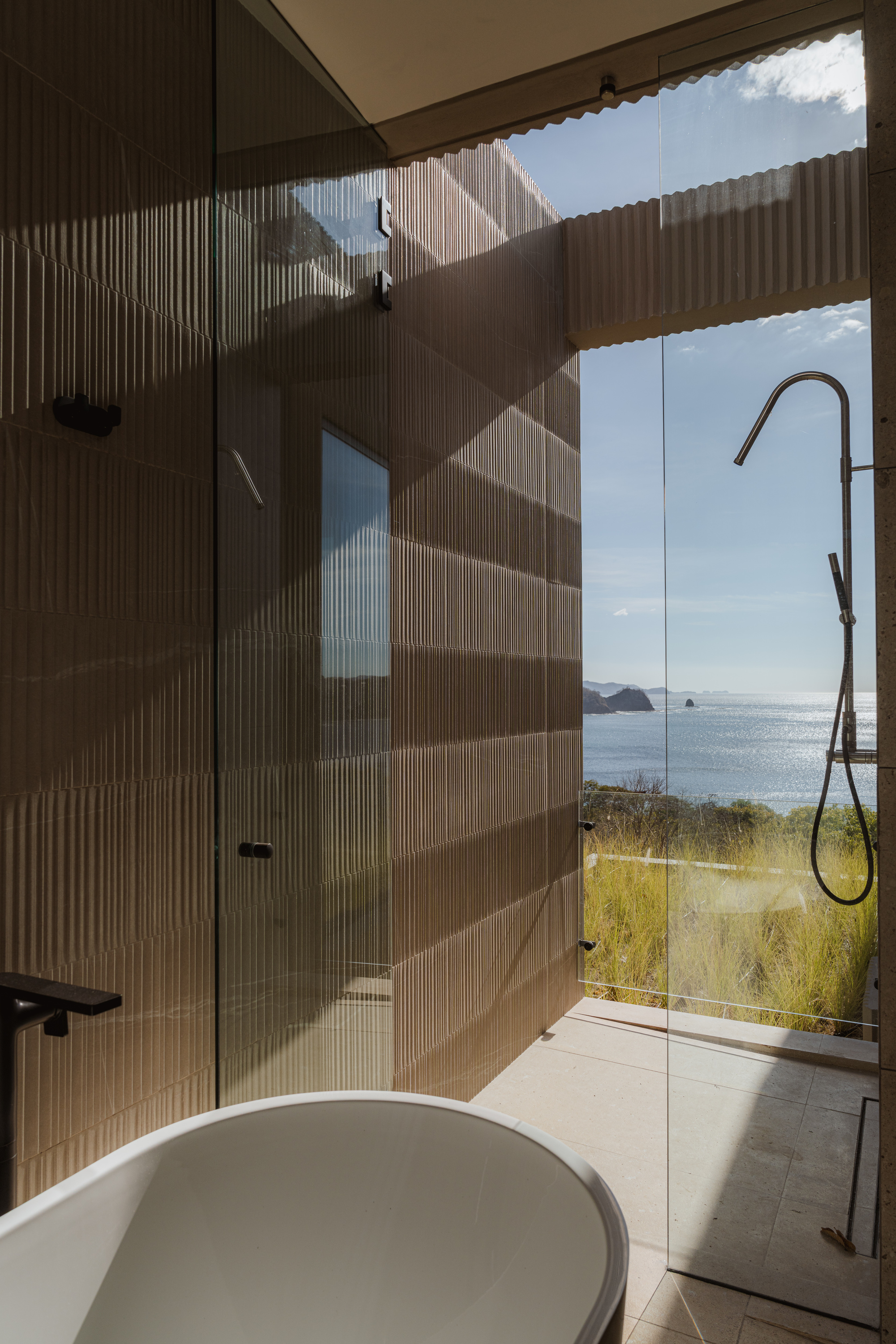 Bathroom with freestanding tub and ribbed timber wall opening to ocean view through glass doors