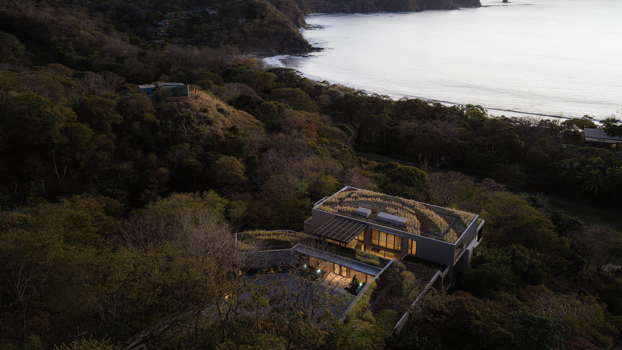 Aerial view of planted roof terraces nestled into hillside above coastal bay at dusk