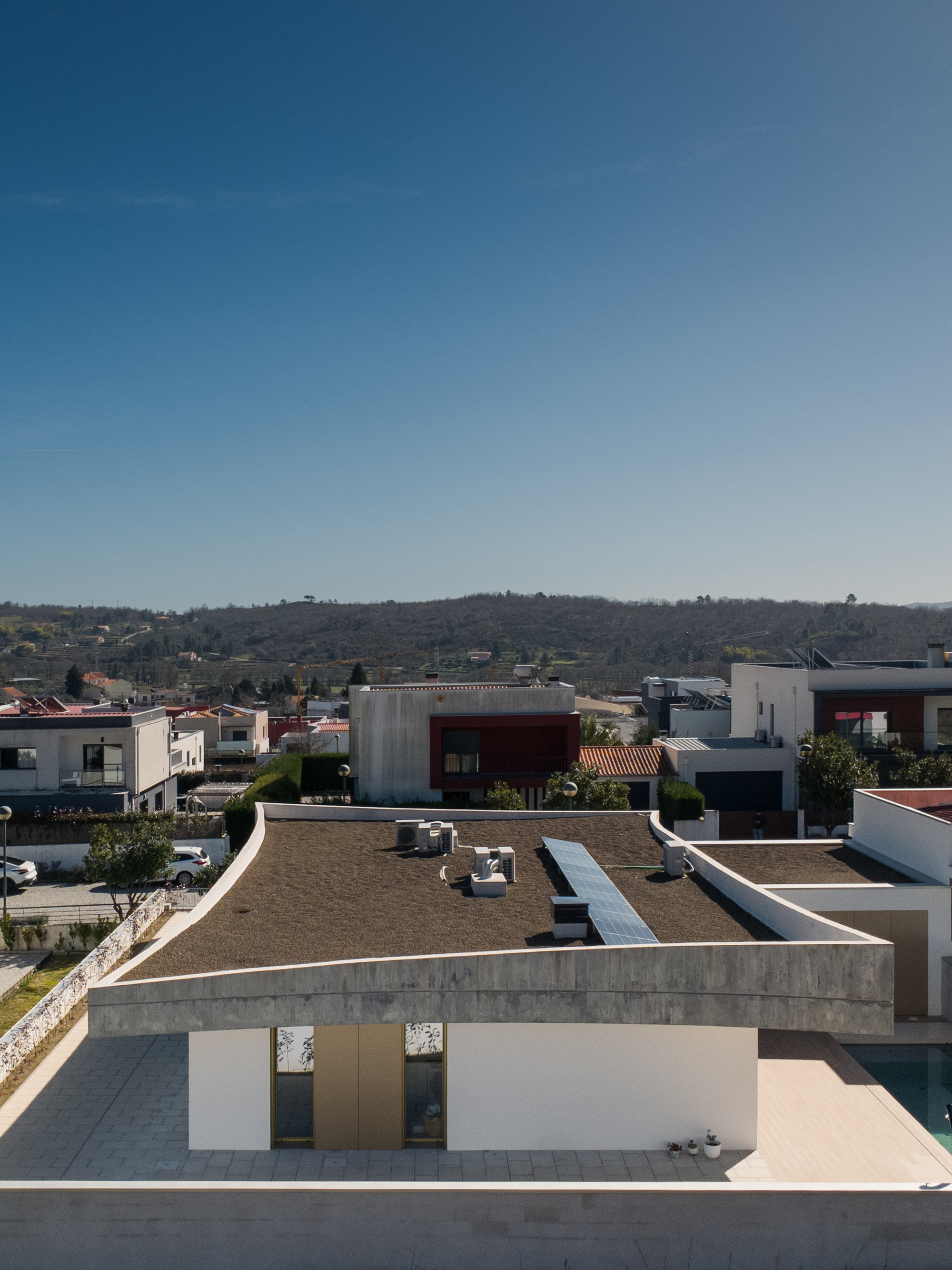Elevated view of the gravel roof terrace with concrete parapet and hillside neighborhood beyond under clear sky