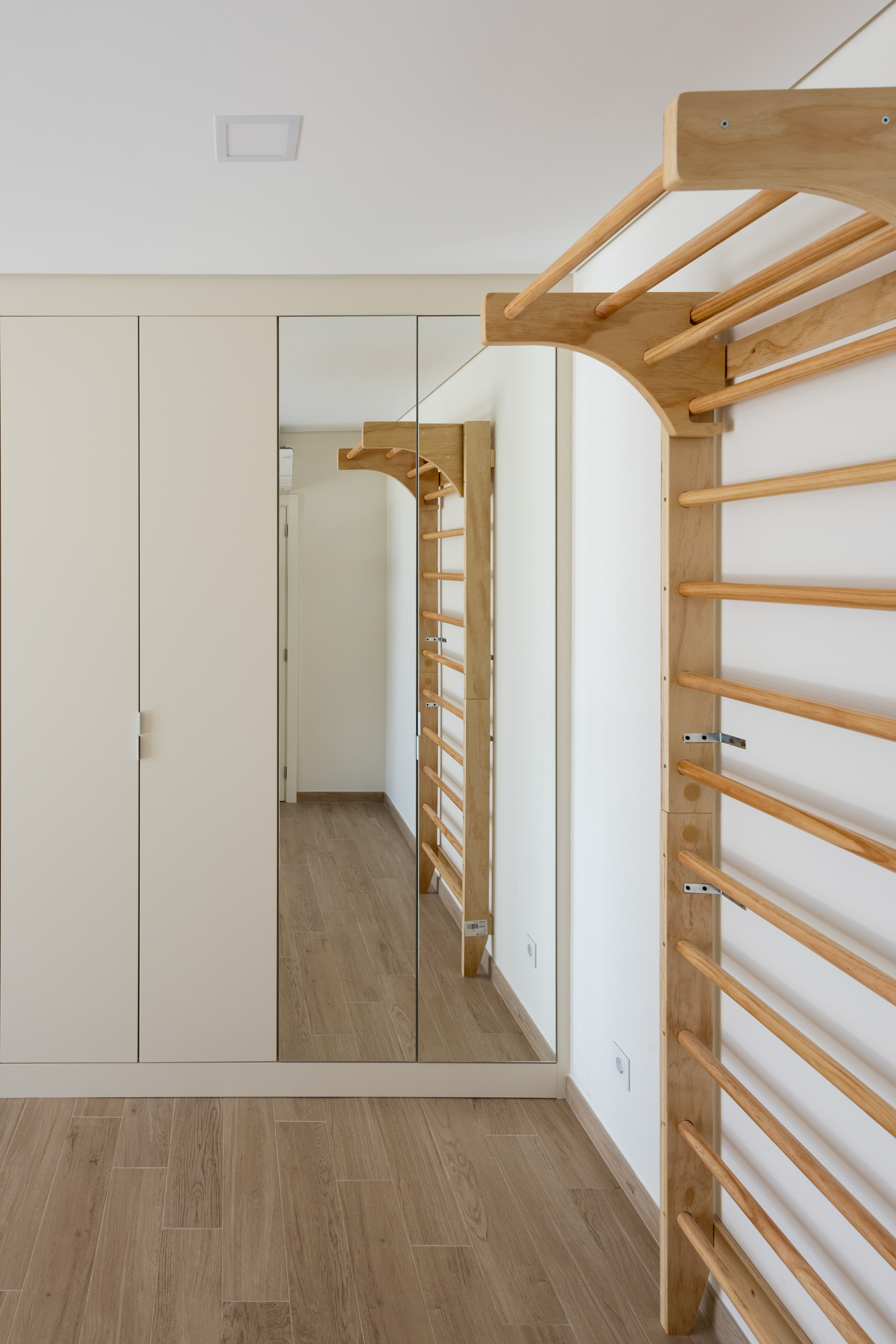 Timber wall bars and overhead monkey bars beside a mirrored wardrobe in a white-walled room