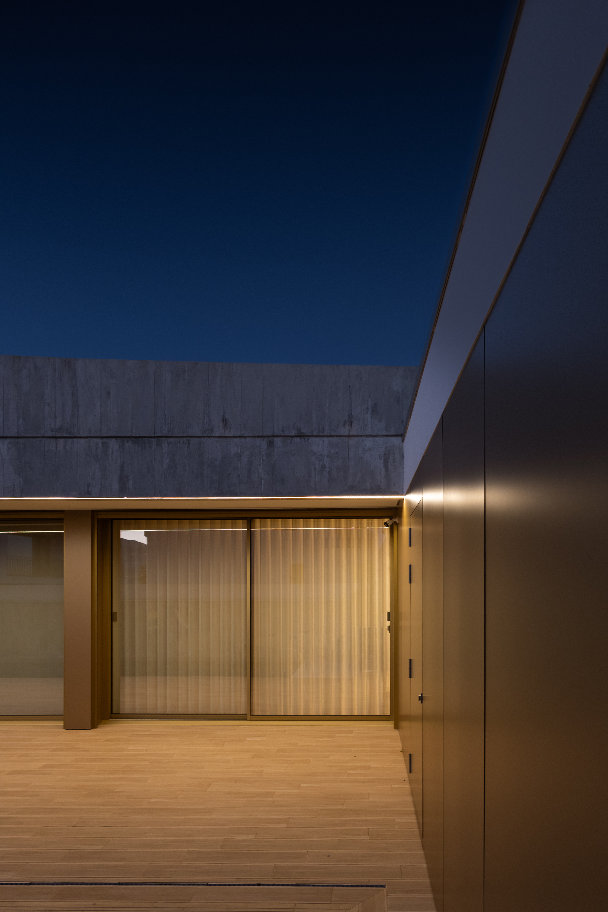 Covered timber deck with sliding glass doors and vertical wood-slat screens at twilight