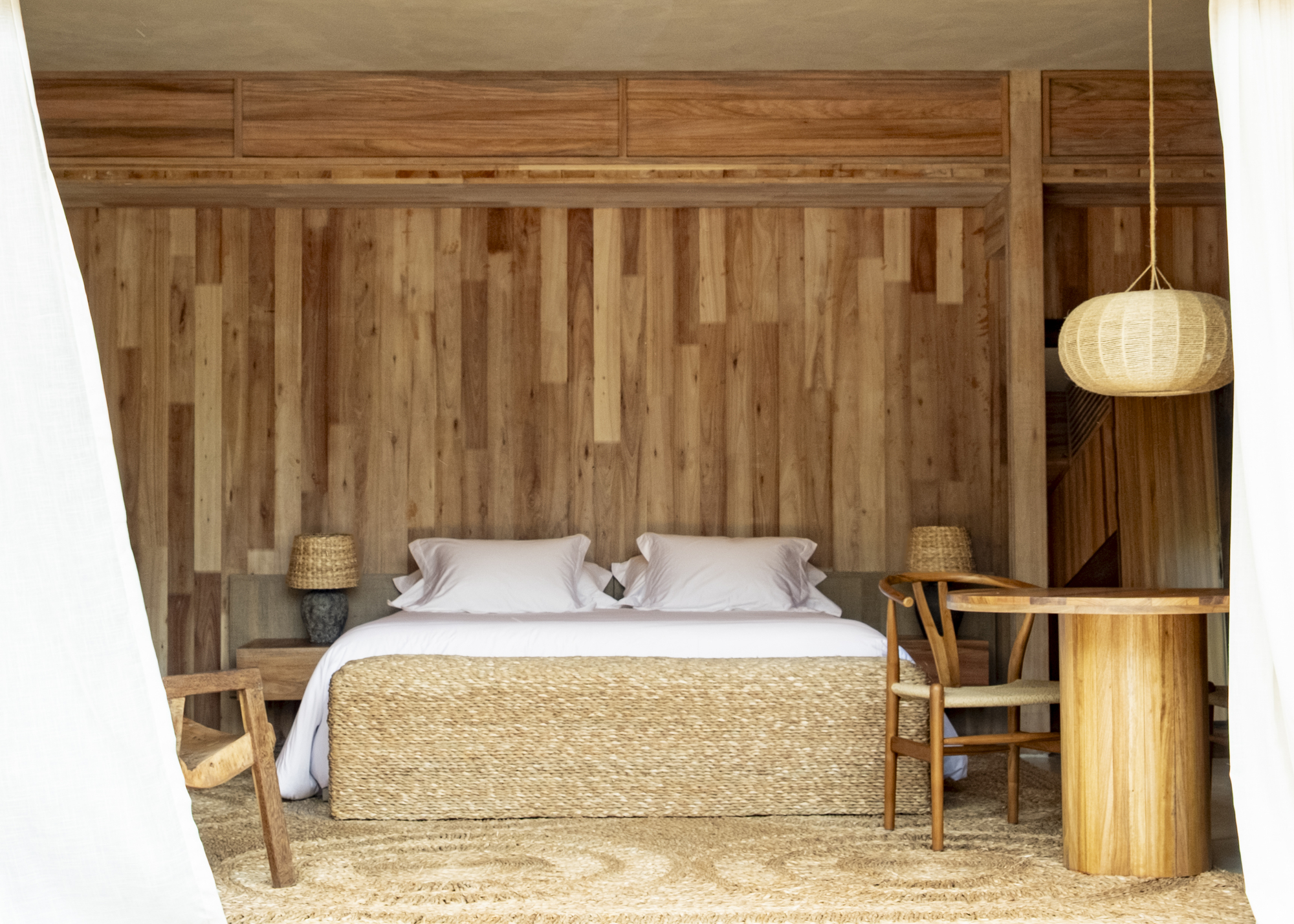 Built-in bed niche framed by vertical wood panels and a woven pendant light hanging overhead