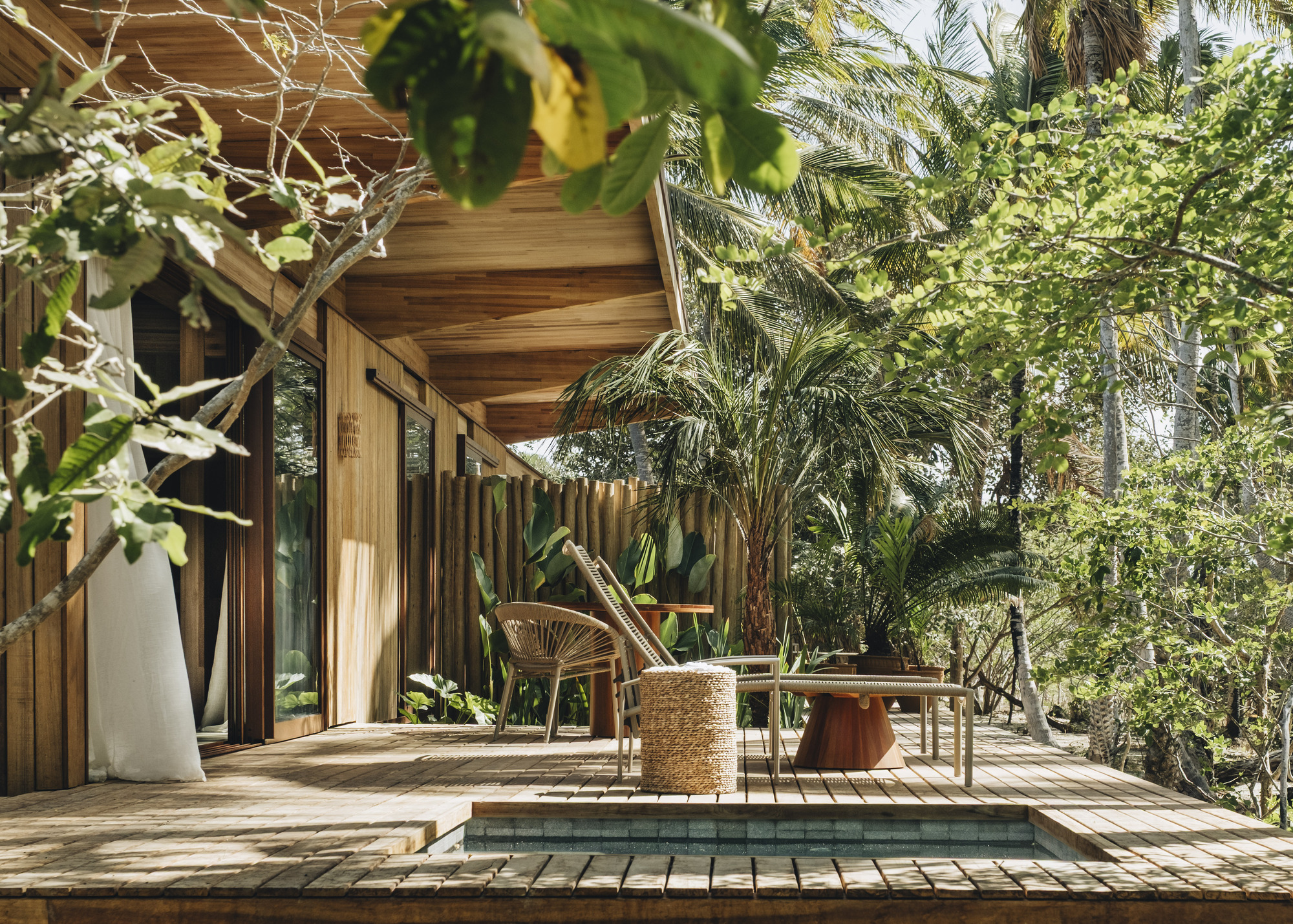 Wooden deck with shallow pool bordered by vertical slatted facade and dense tropical plantings