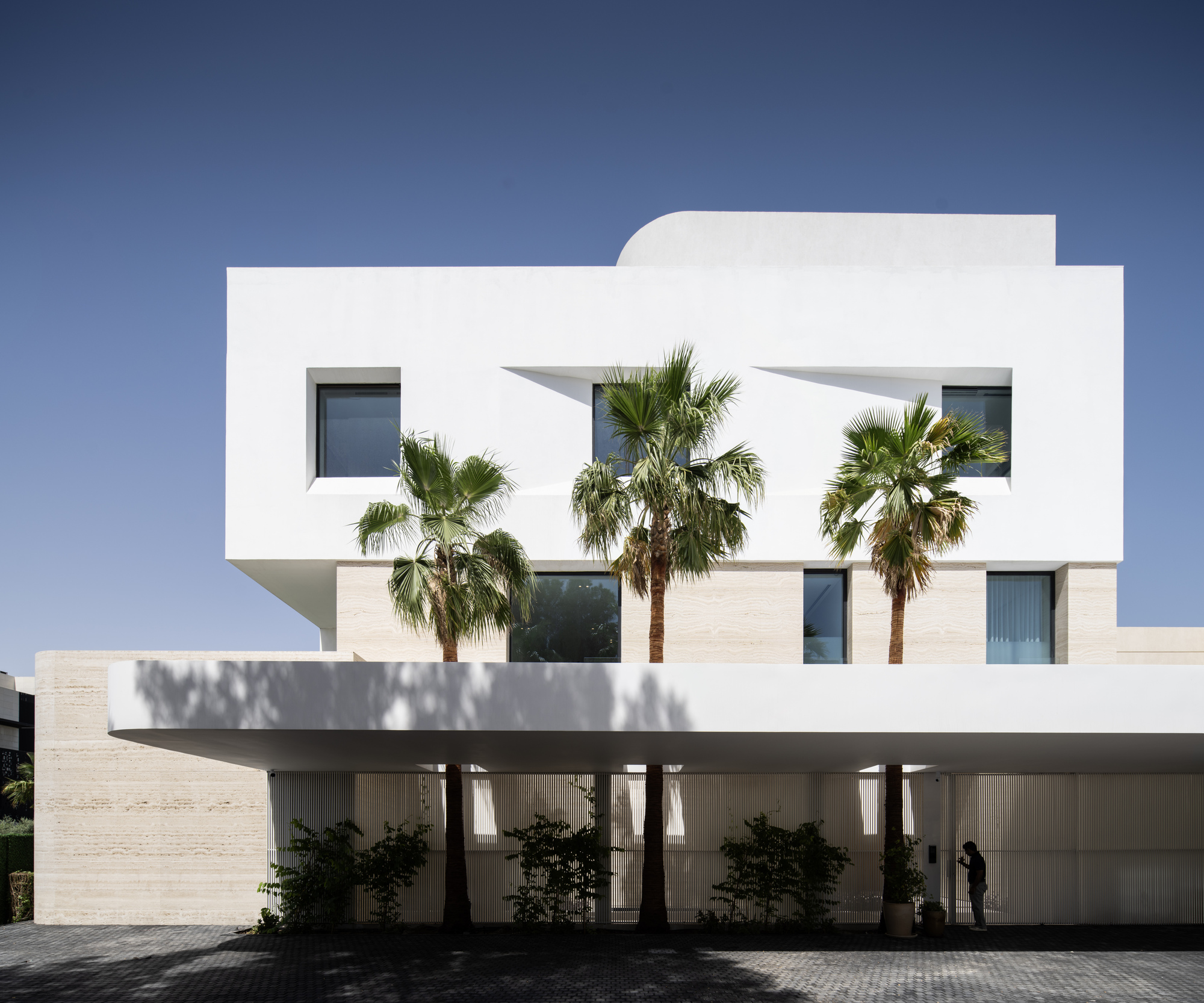 White stucco facade with angled underside and palm trees set against a clear blue sky