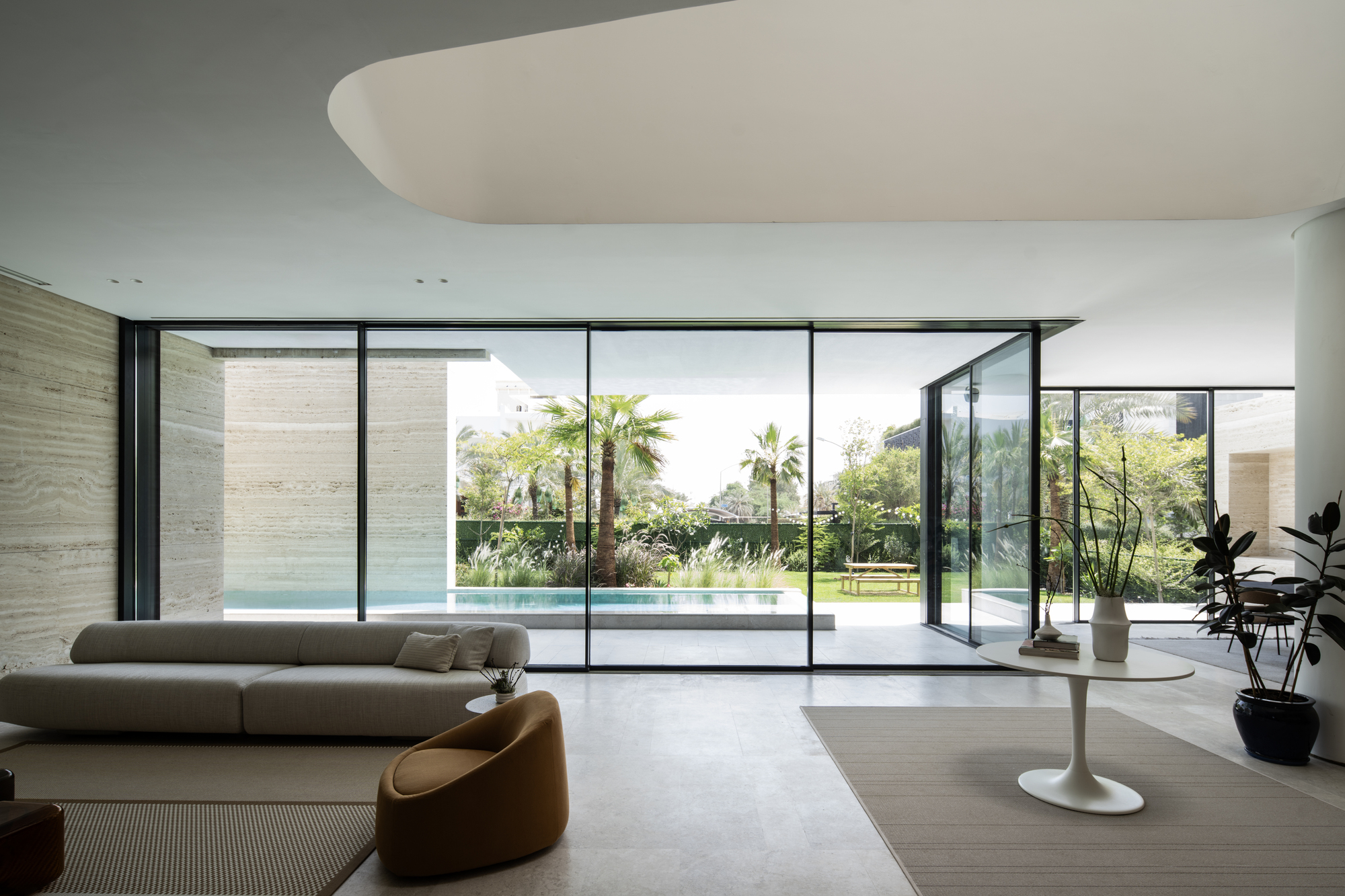 Living room with floor-to-ceiling glazing overlooking pool and palm trees in the garden