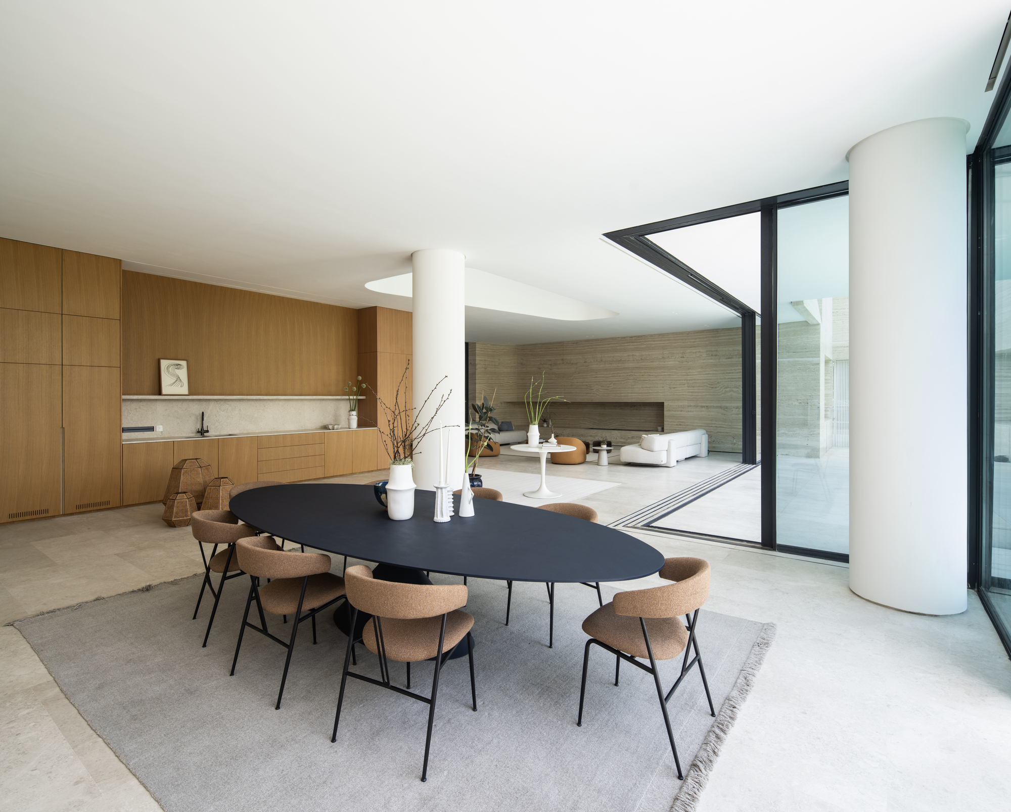 Open-plan interior with black oval dining table beside white cylindrical column and full-height glazing
