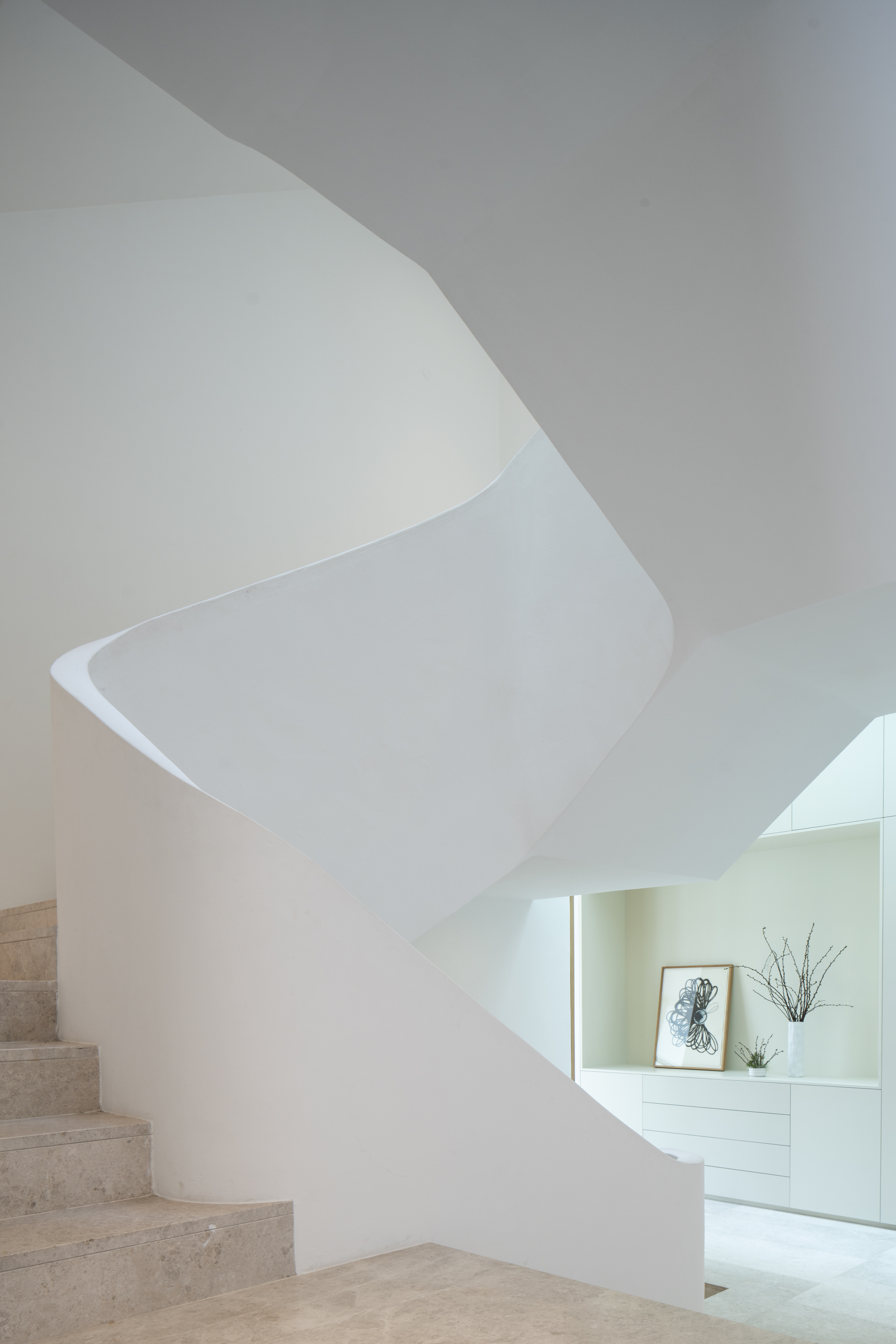 Sculptural white plaster staircase with spiraling wall and travertine treads under soft daylight