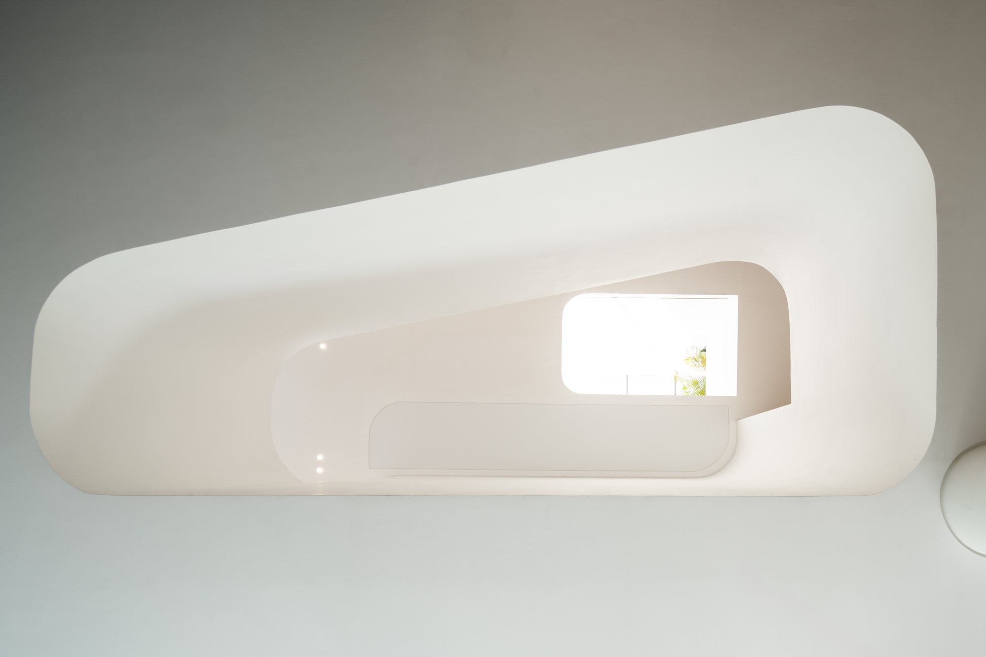 Looking up through the curving white stairwell with rounded opening framing a window above