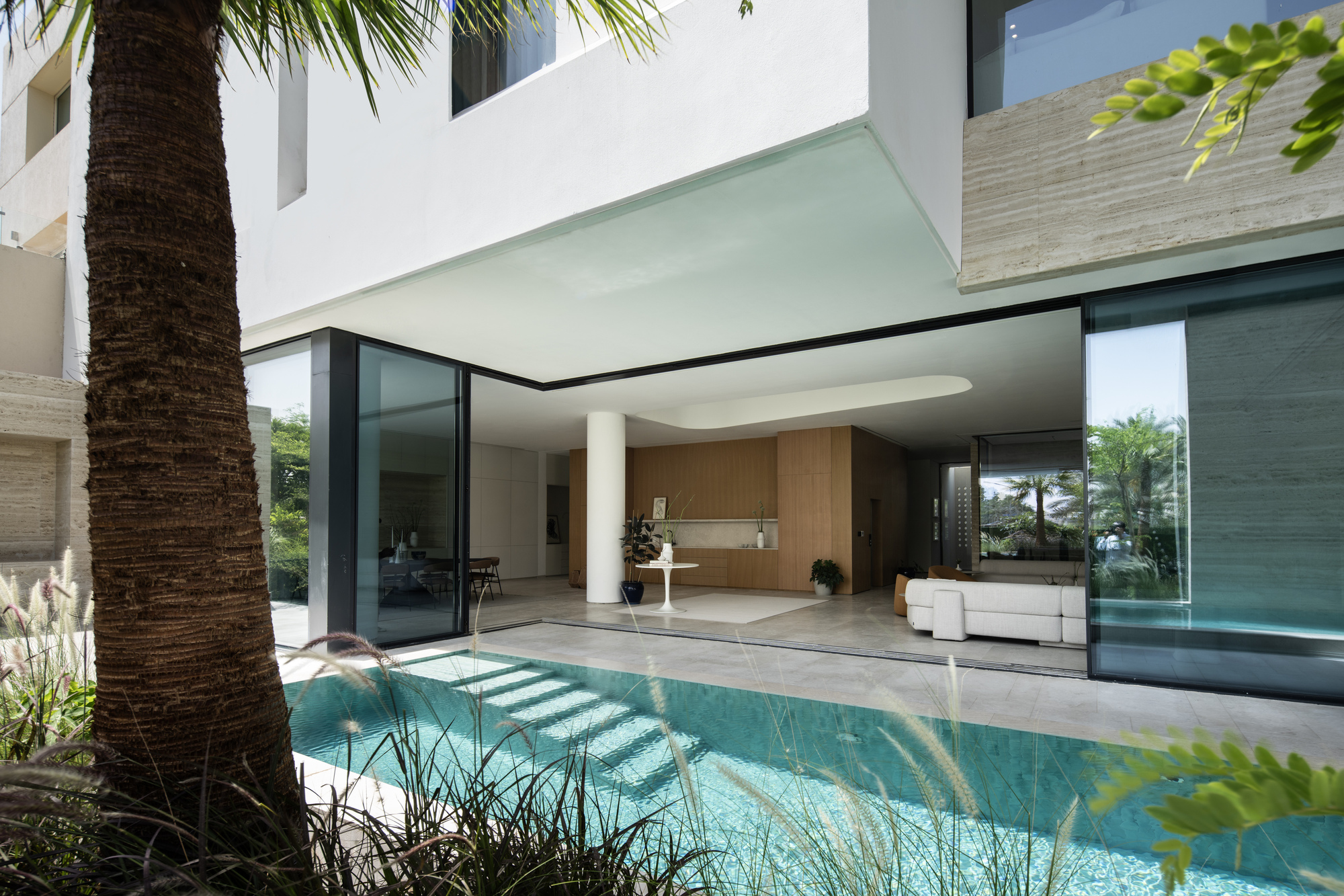 Covered terrace overlooking lap pool with palm trees and sliding glass doors to interior