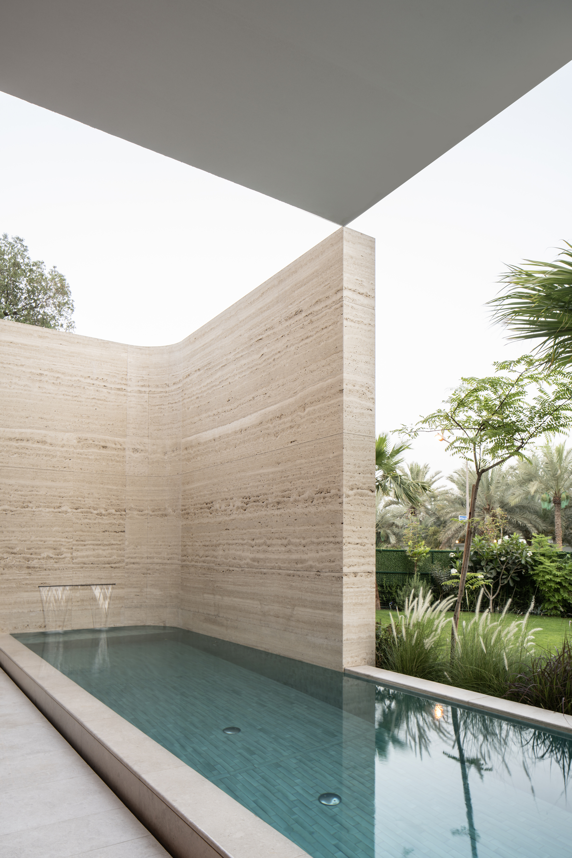 Corner courtyard pool enclosed by horizontal banded travertine walls beneath an angled white overhang