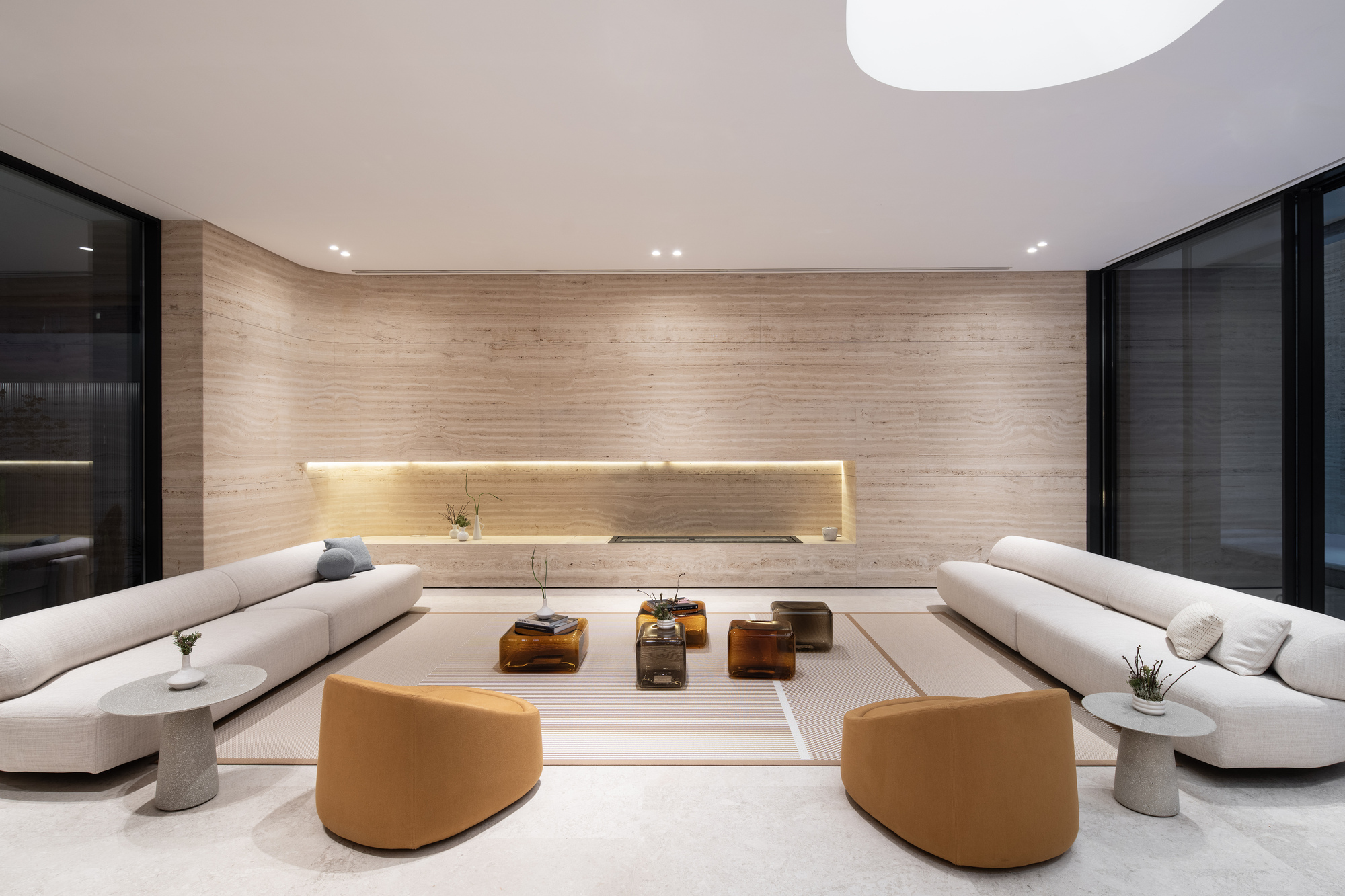 Living room with curved board-formed concrete wall, horizontal light slot and flanking black-framed glass doors