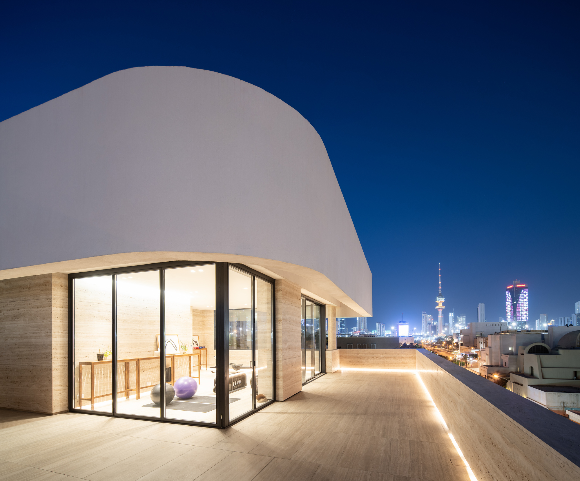 Rooftop terrace with curved white volume and glazed door opening under deep blue night sky