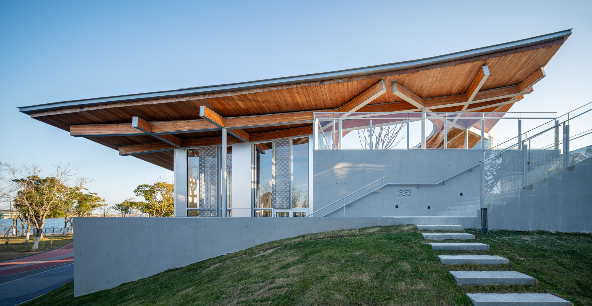 Elevated pavilion with cantilevered timber soffit roof and white concrete stepped path through sloped lawn