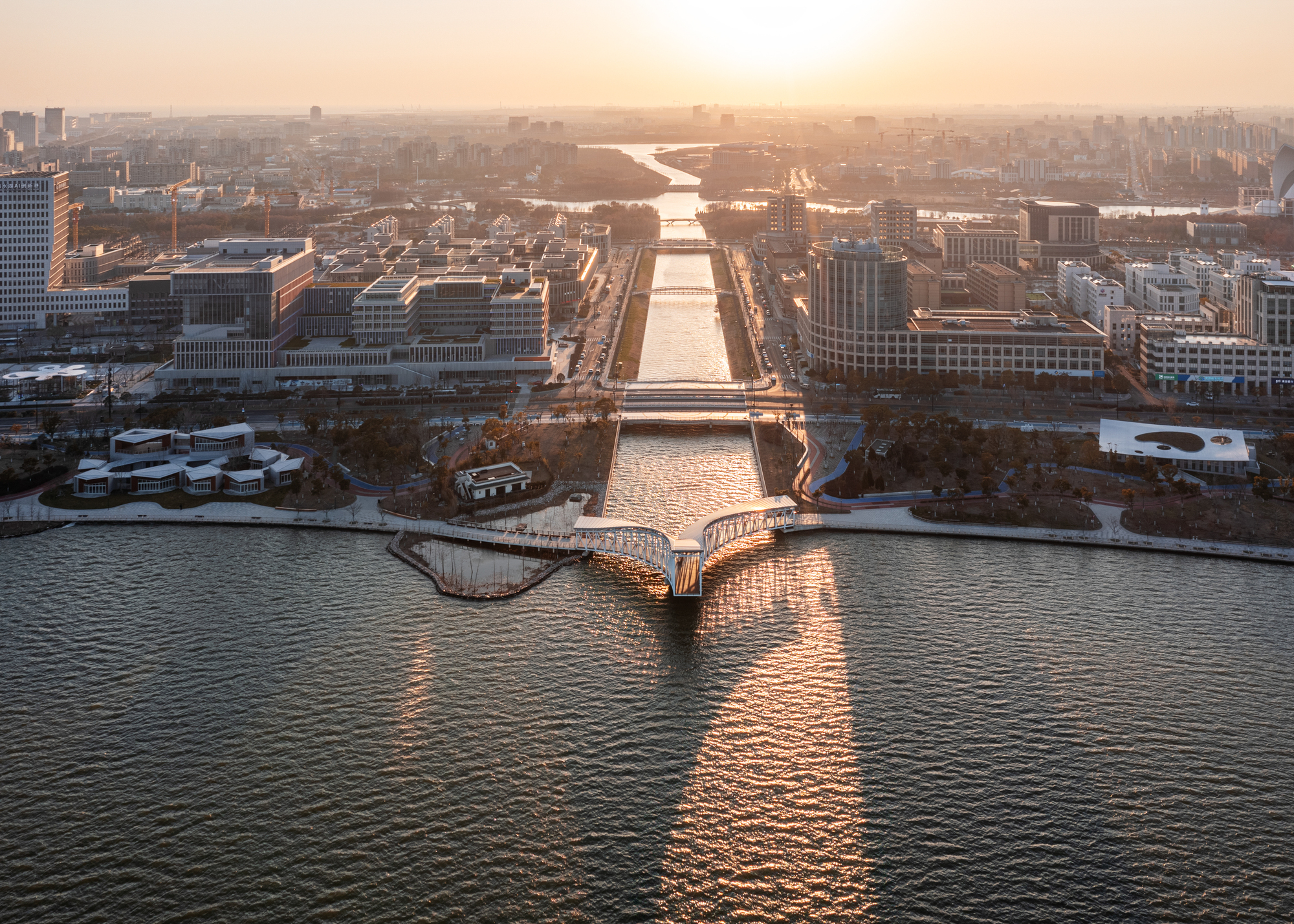 Aerial view of pedestrian bridge extending across water toward urban canal at golden hour