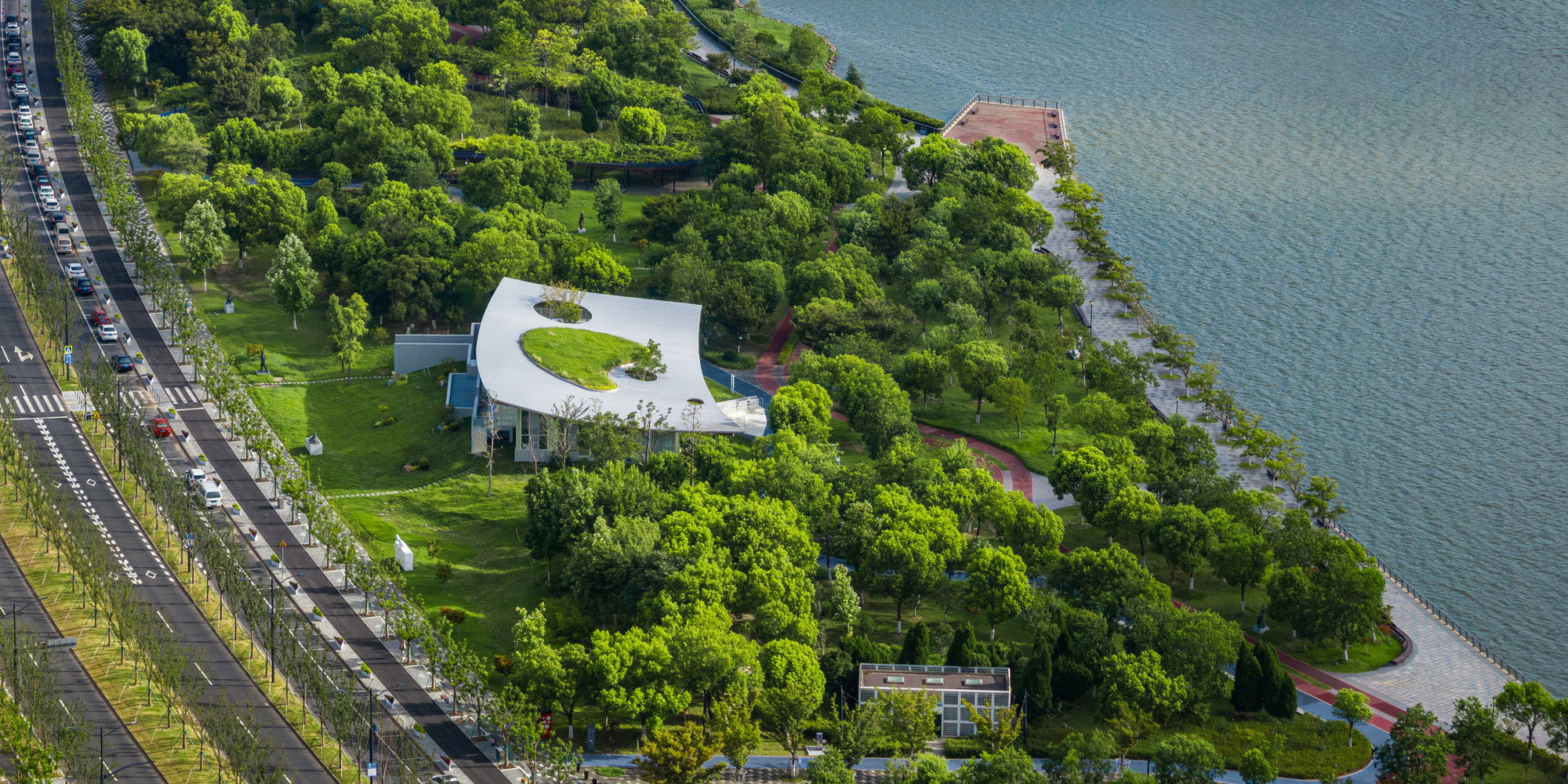 Drone view of curved white roof with central planted courtyard nestled in waterfront park