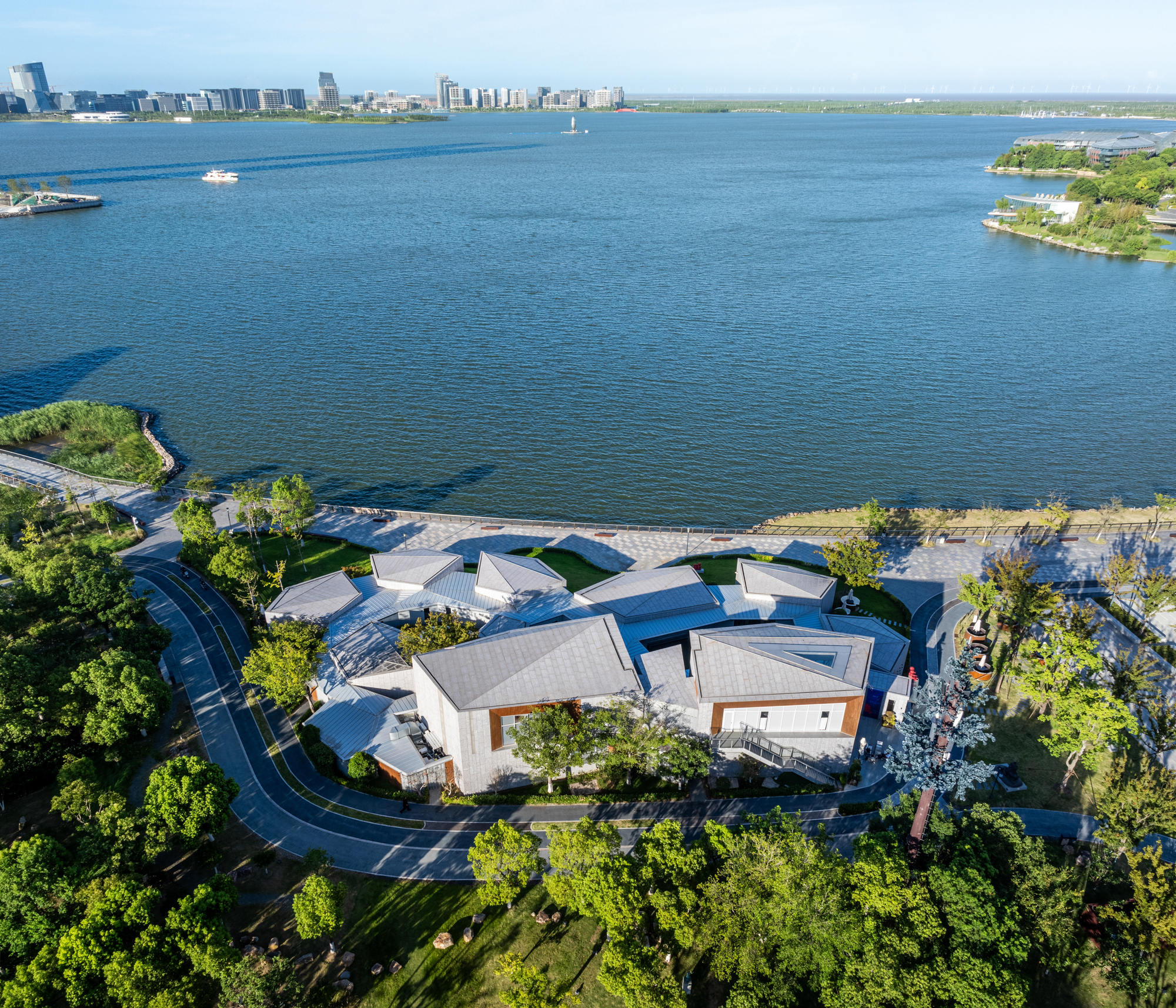 Aerial view of clustered pavilions with angular roofs along landscaped waterfront promenade
