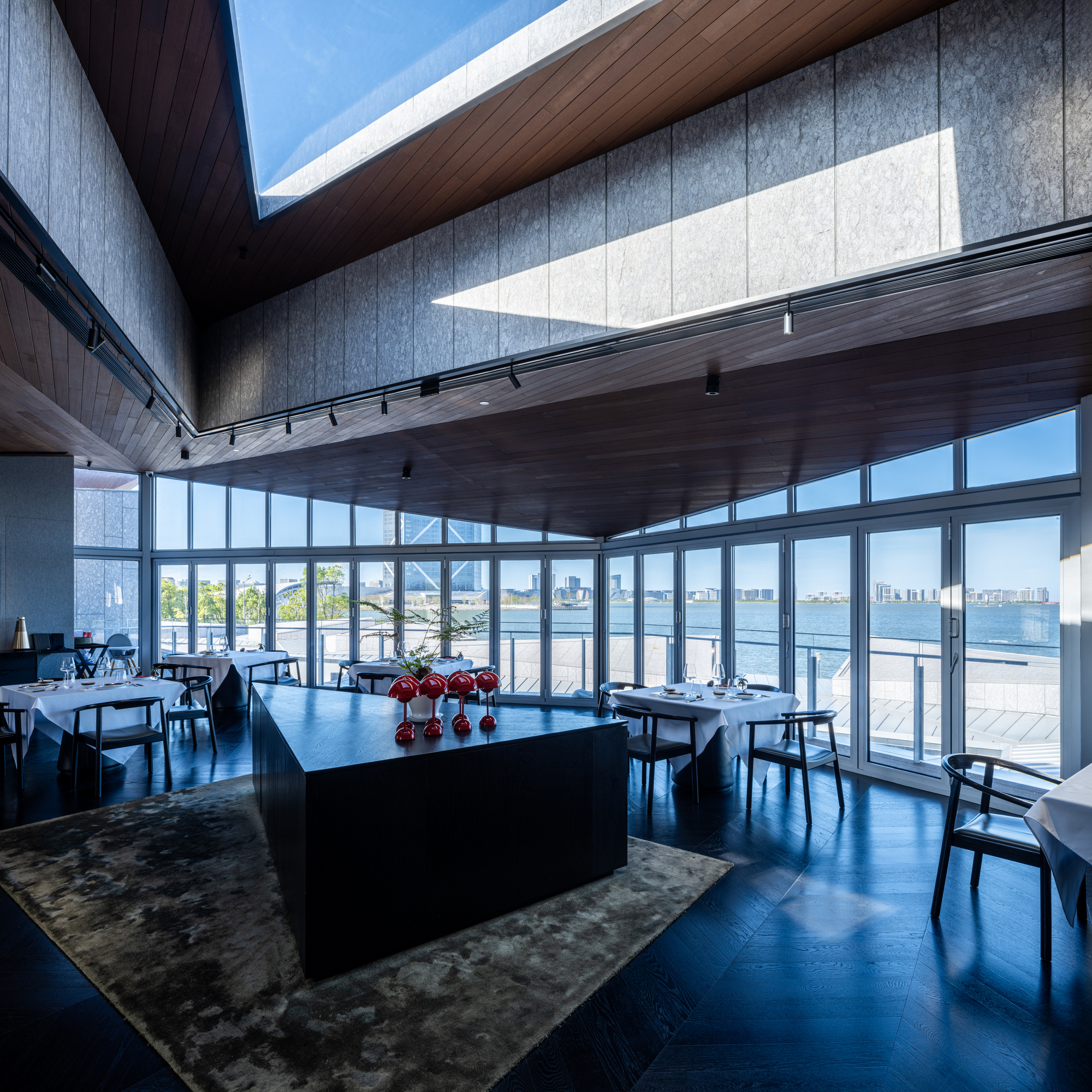 Dining space with timber ceiling and floor-to-ceiling glazing overlooking water and distant skyline