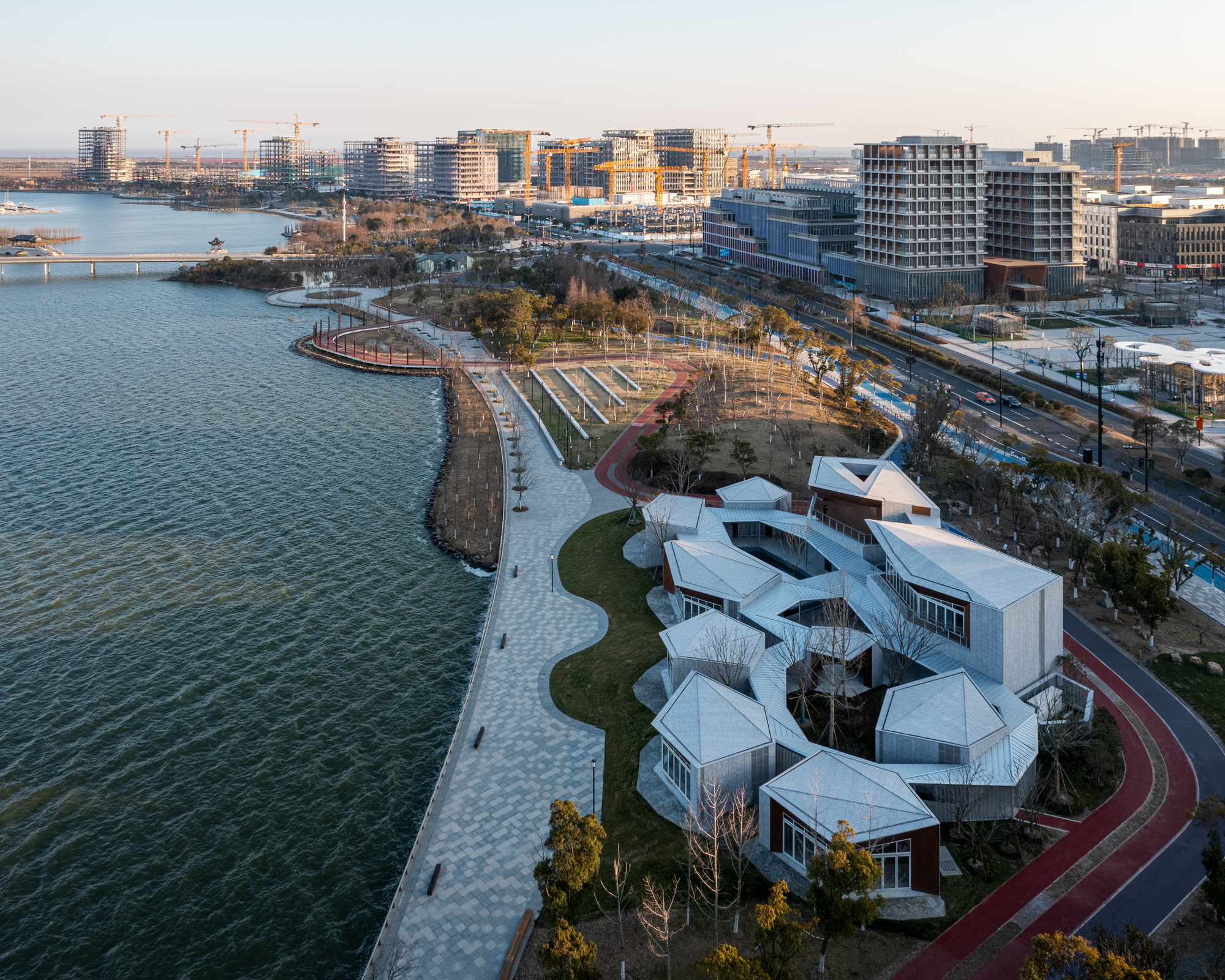 Aerial view of cloverleaf-shaped white roof volumes clustered along waterfront park at dusk
