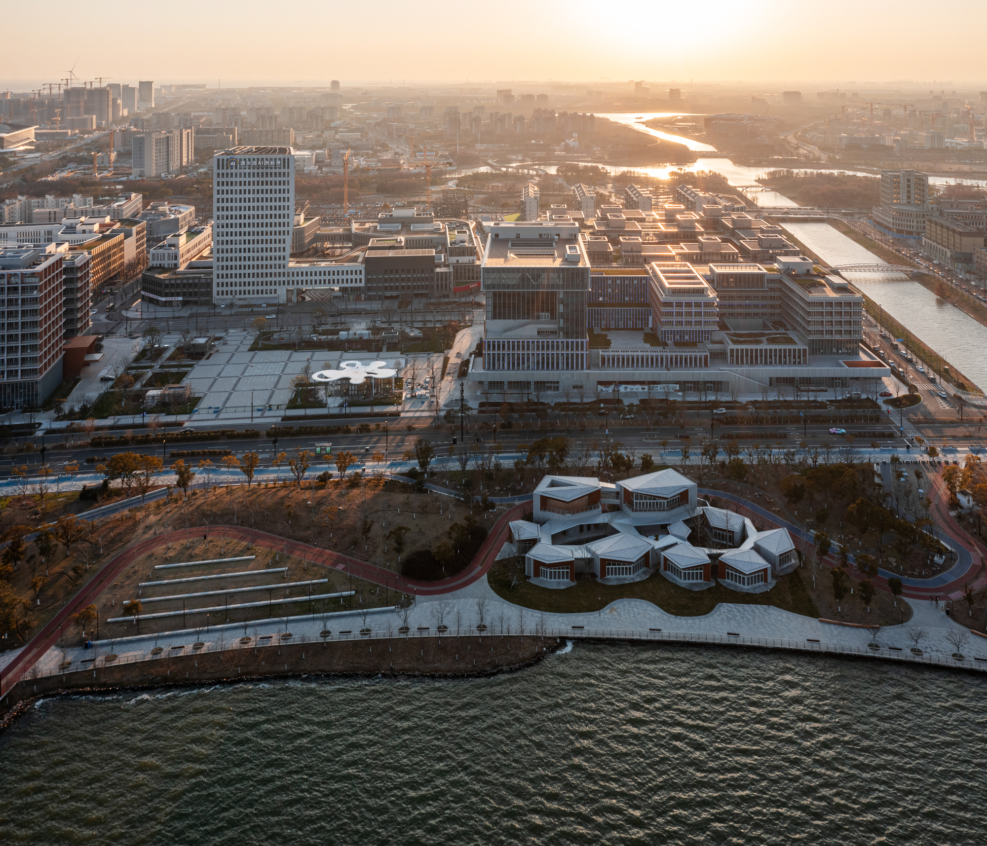 Drone view of the lobed roof forms at water's edge with city towers and river in golden hour light