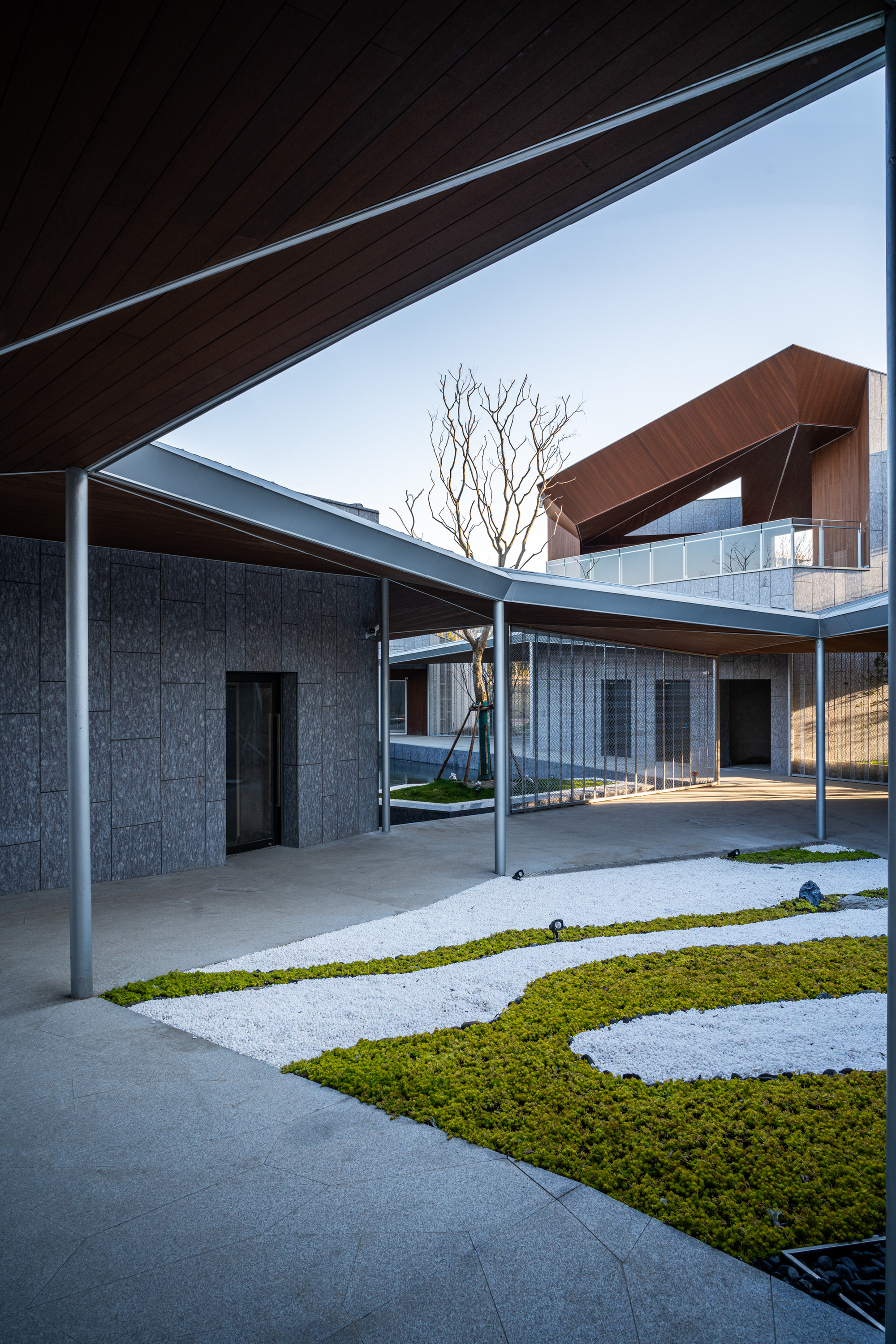 Courtyard with geometric grass and gravel ground pattern framed by timber soffits and bare tree