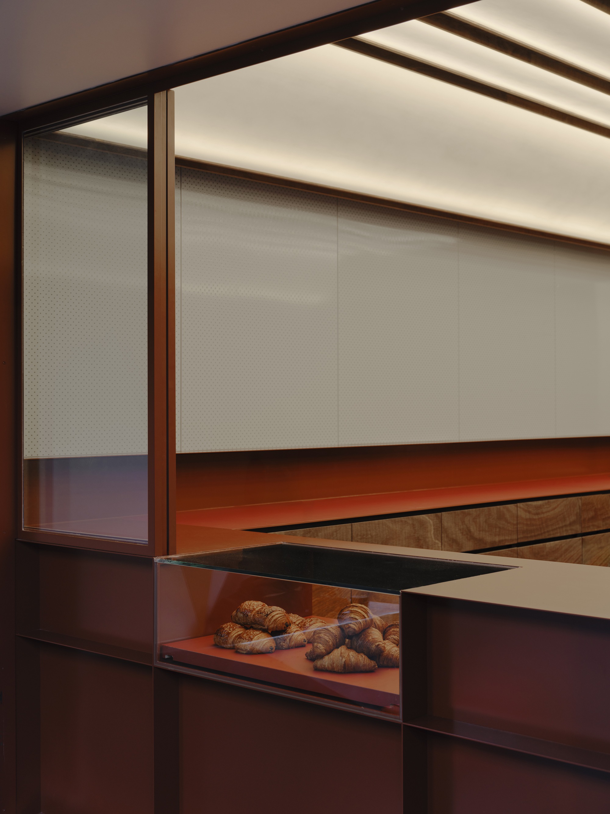 Close-up of the translucent perforated panels and red metal counter with pastries displayed below