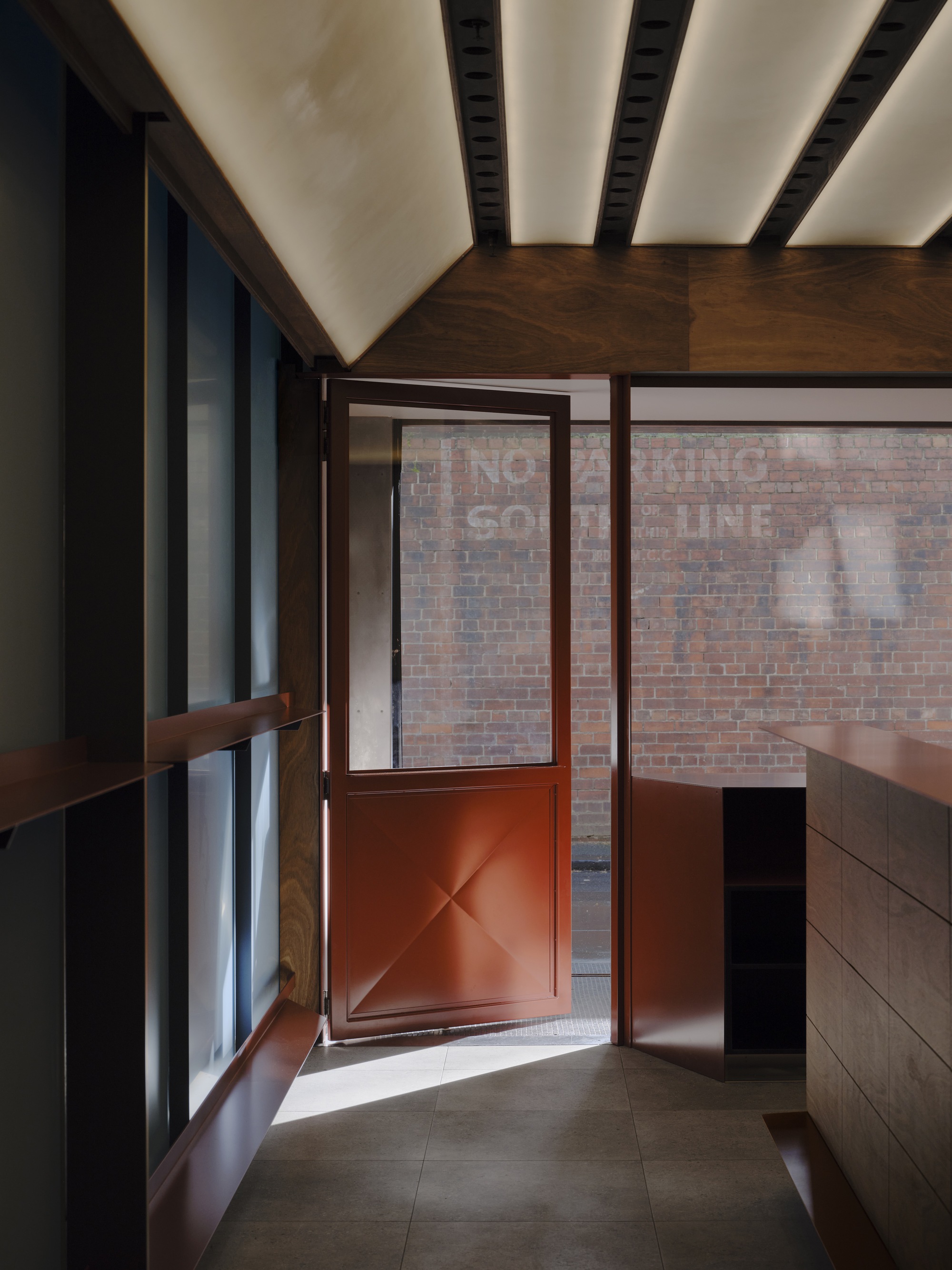 View toward the red metal door opening onto the brick courtyard under the timber canopy