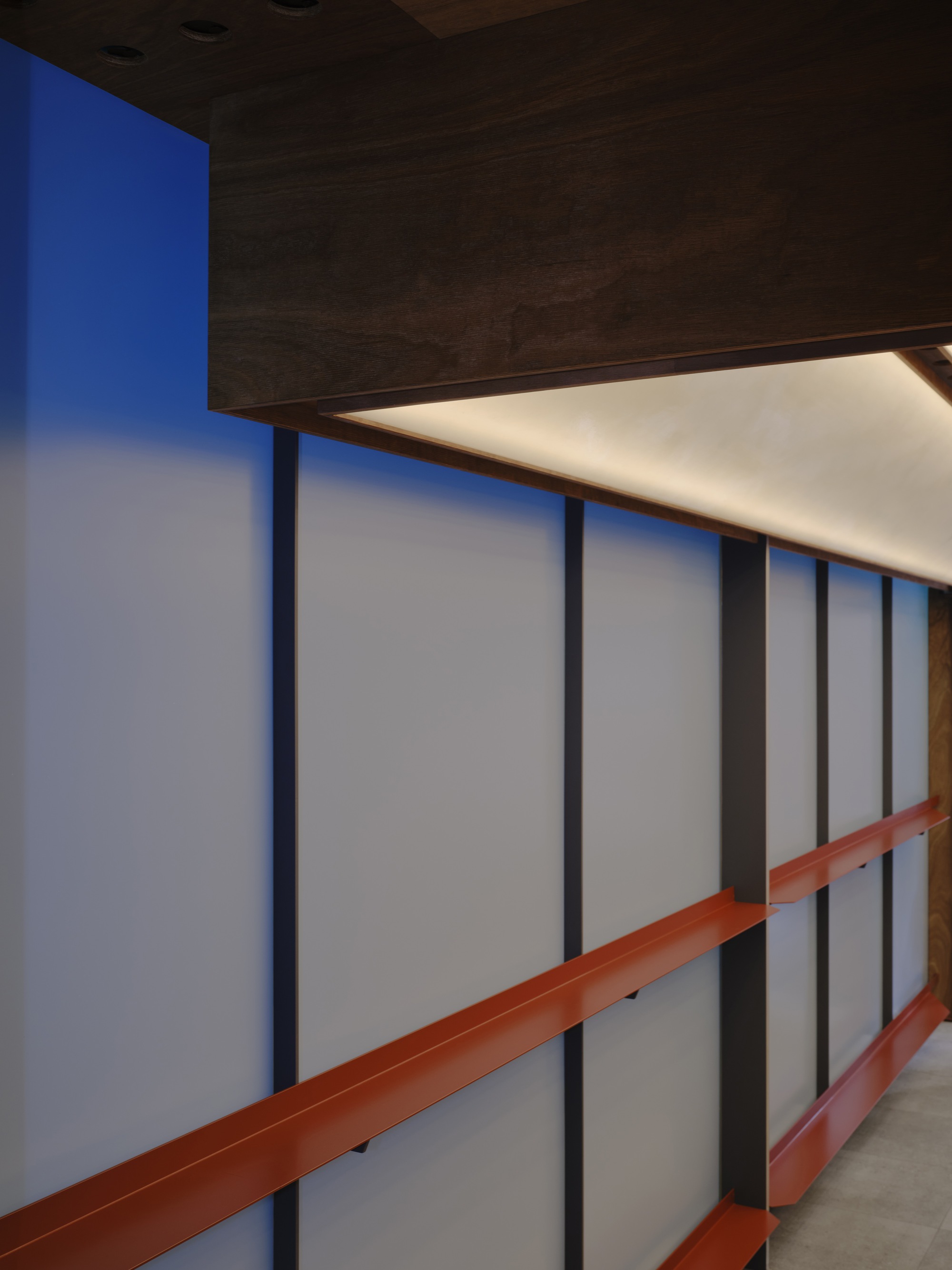 Dark timber volume suspended above the frosted glass wall with integrated ceiling lighting
