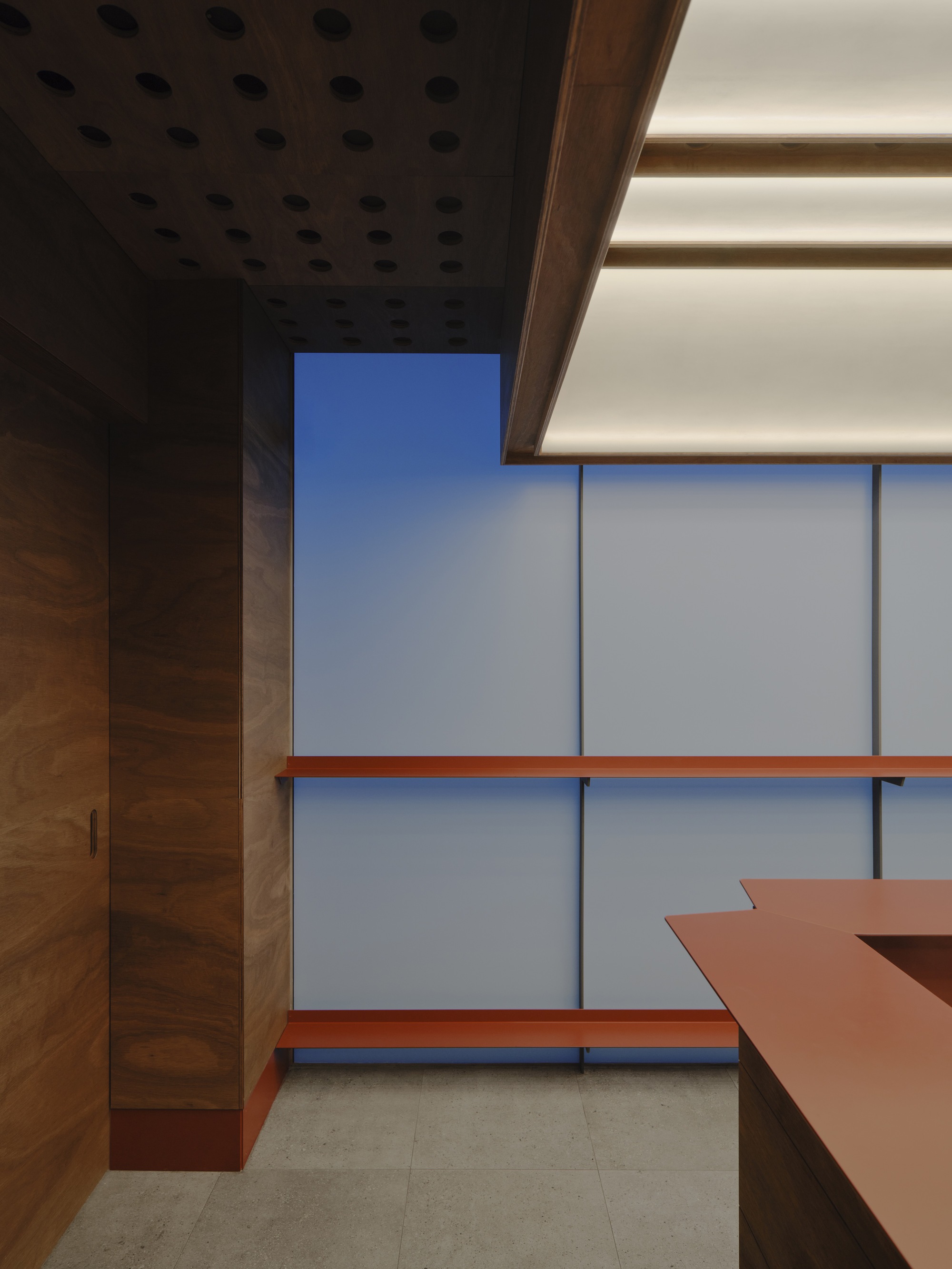 Corner view showing perforated ceiling panel, timber cabinetry and the layered glass and copper elements