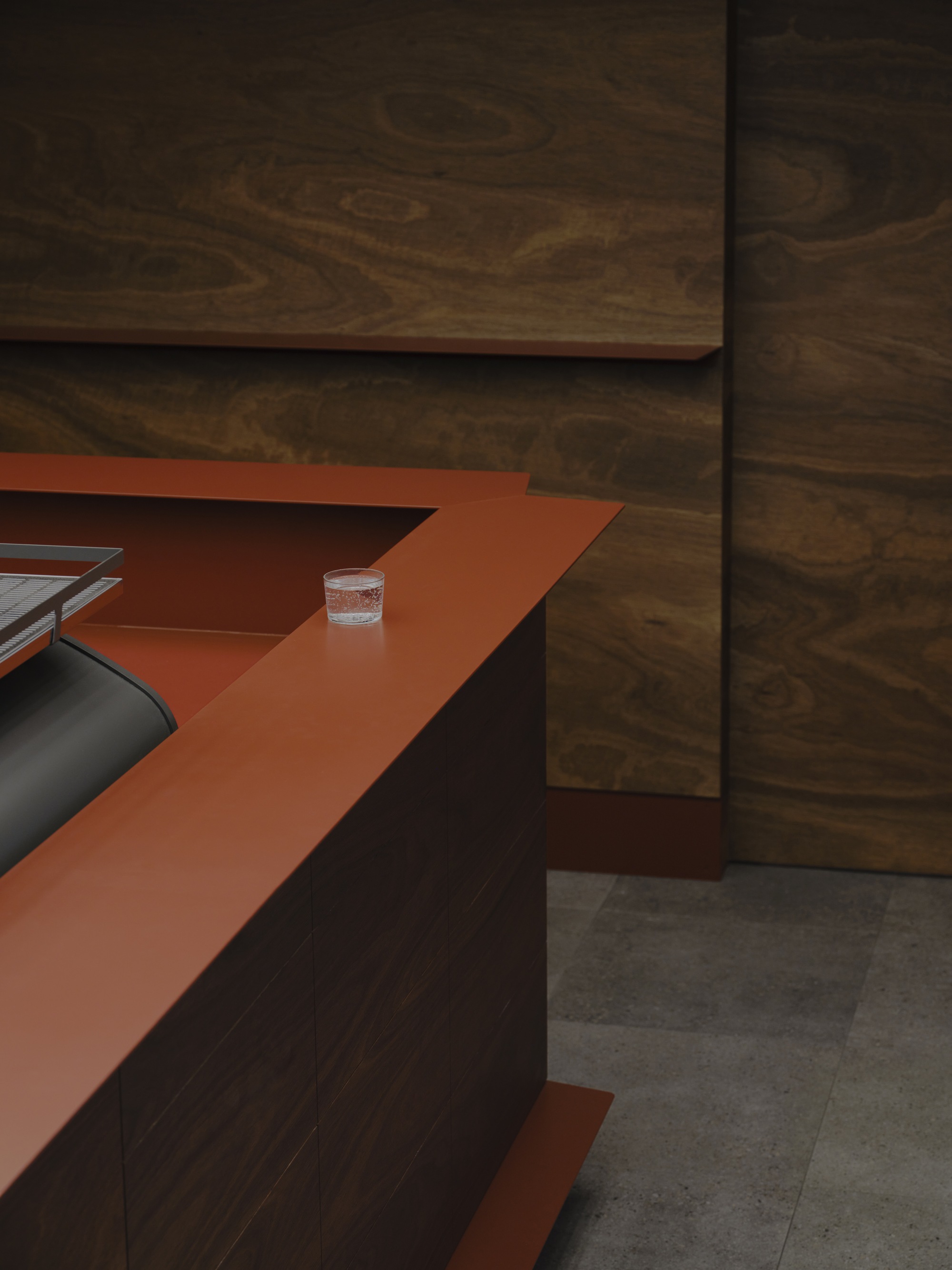 Orange terracotta worktop meeting dark timber wall panels with a glass of water
