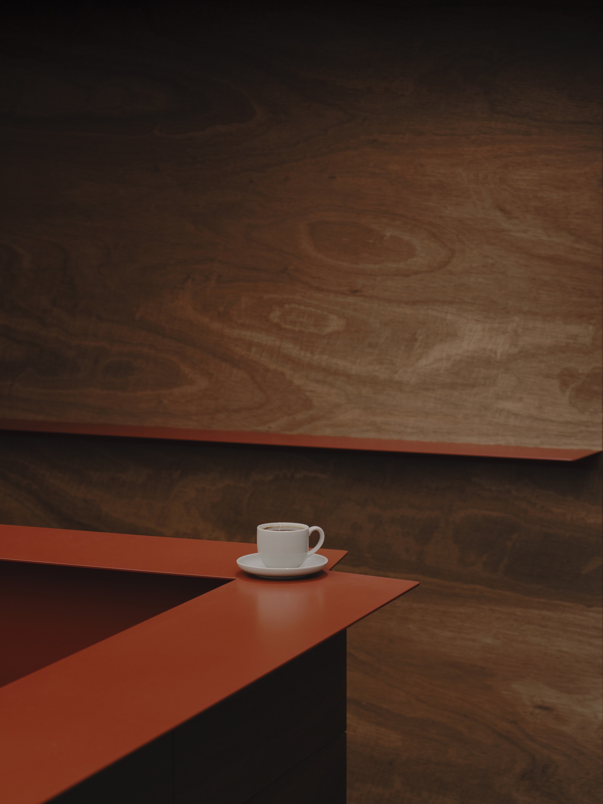 White coffee cup on terracotta counter beneath suspended timber ceiling panel in dim light