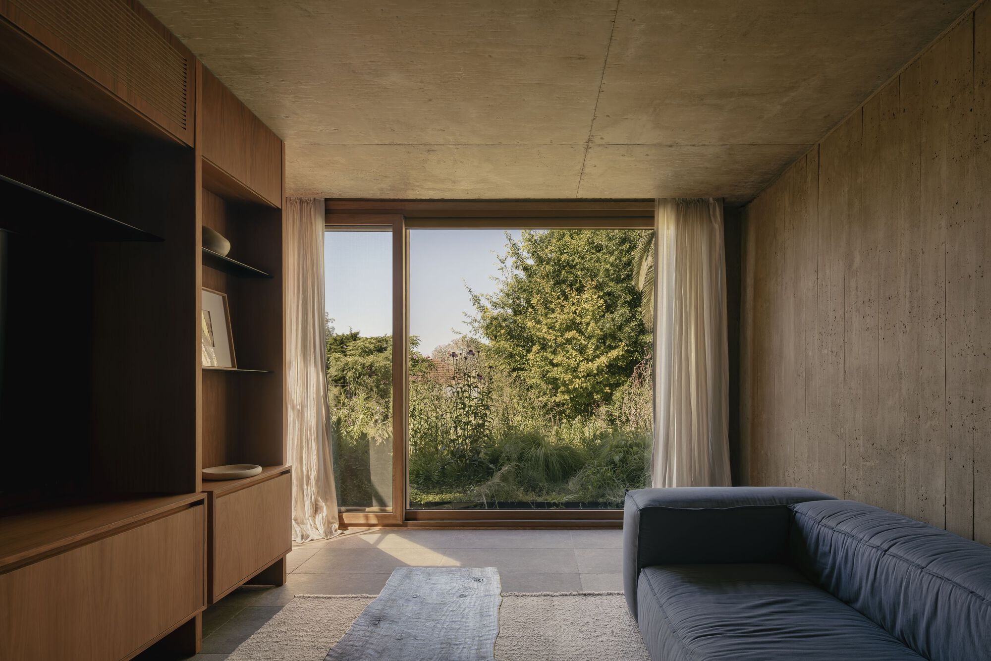 Living room with board-marked concrete walls and timber joinery framing glazed corner window