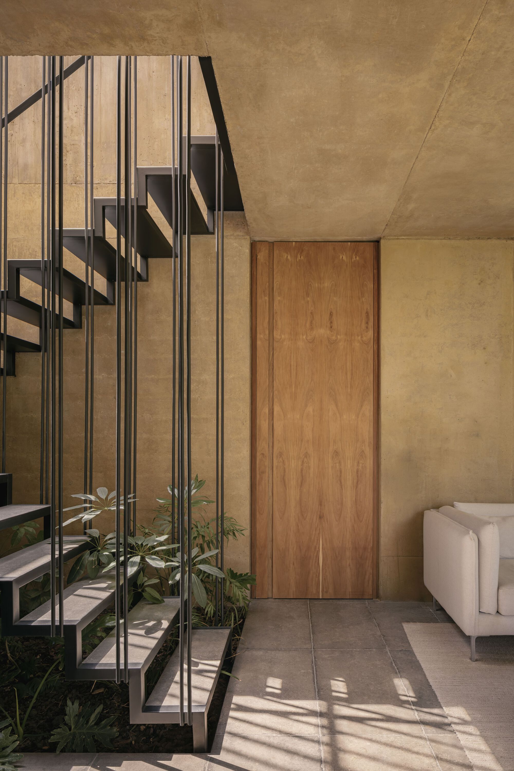 Open-tread staircase with vertical metal balusters casting shadows on stone floor beneath concrete soffit