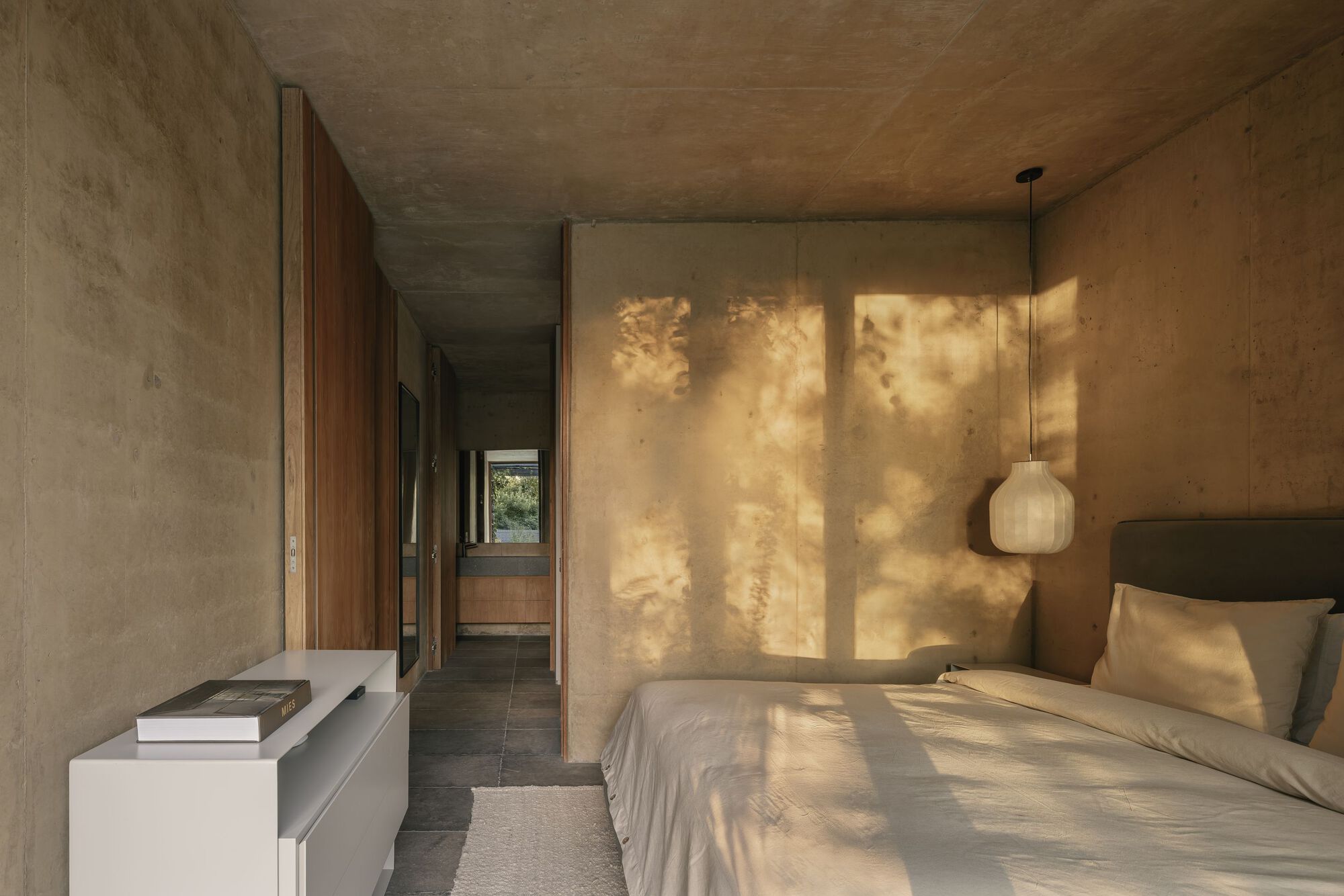 Bedroom corridor with dappled sunlight filtering through exterior louvers onto textured plaster wall