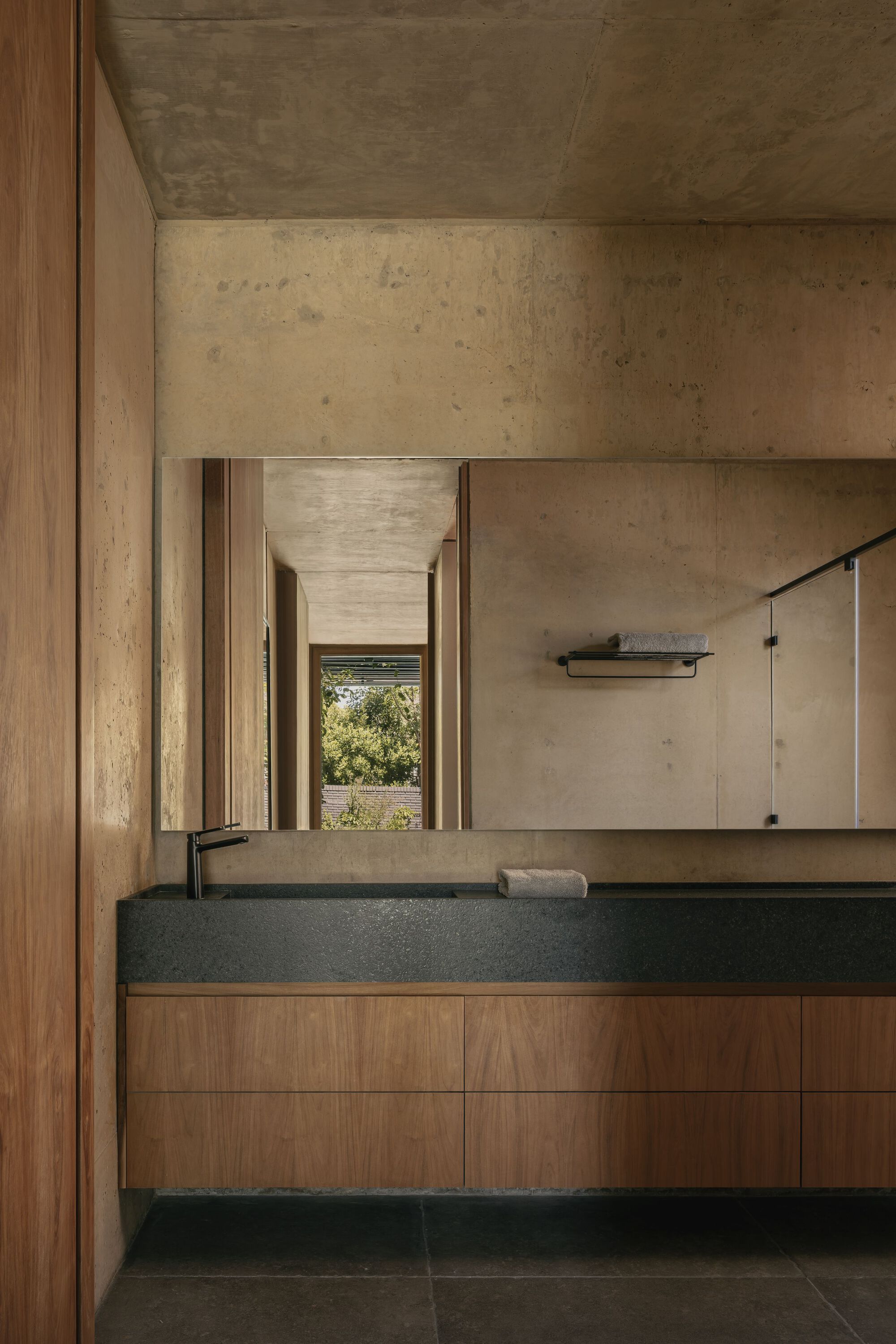 Bathroom vanity with timber cabinetry and black stone sink beneath exposed concrete ceiling