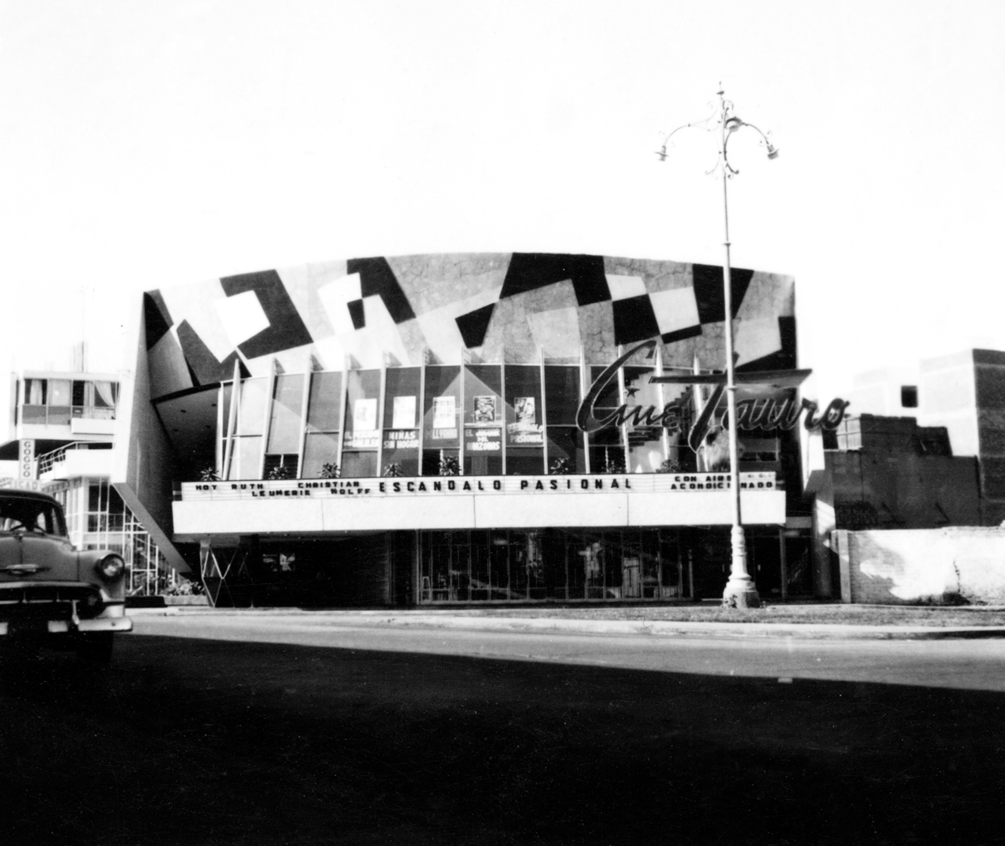 Street view of the cinema facade with geometric roofline and marquee lit by a streetlamp at dusk