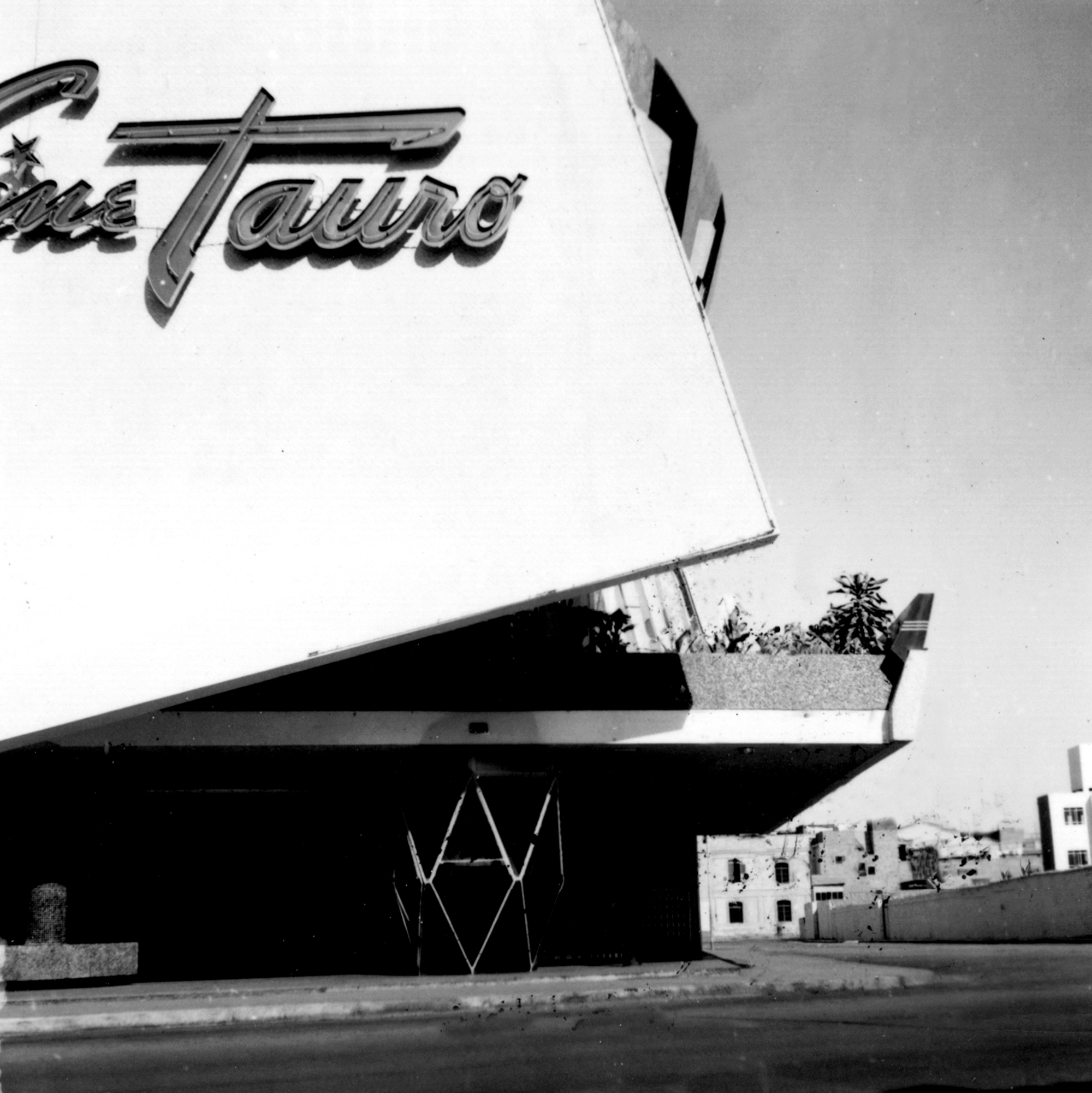 Detail of the cantilevered canopy and signage against the white facade with a palm tree visible beyond