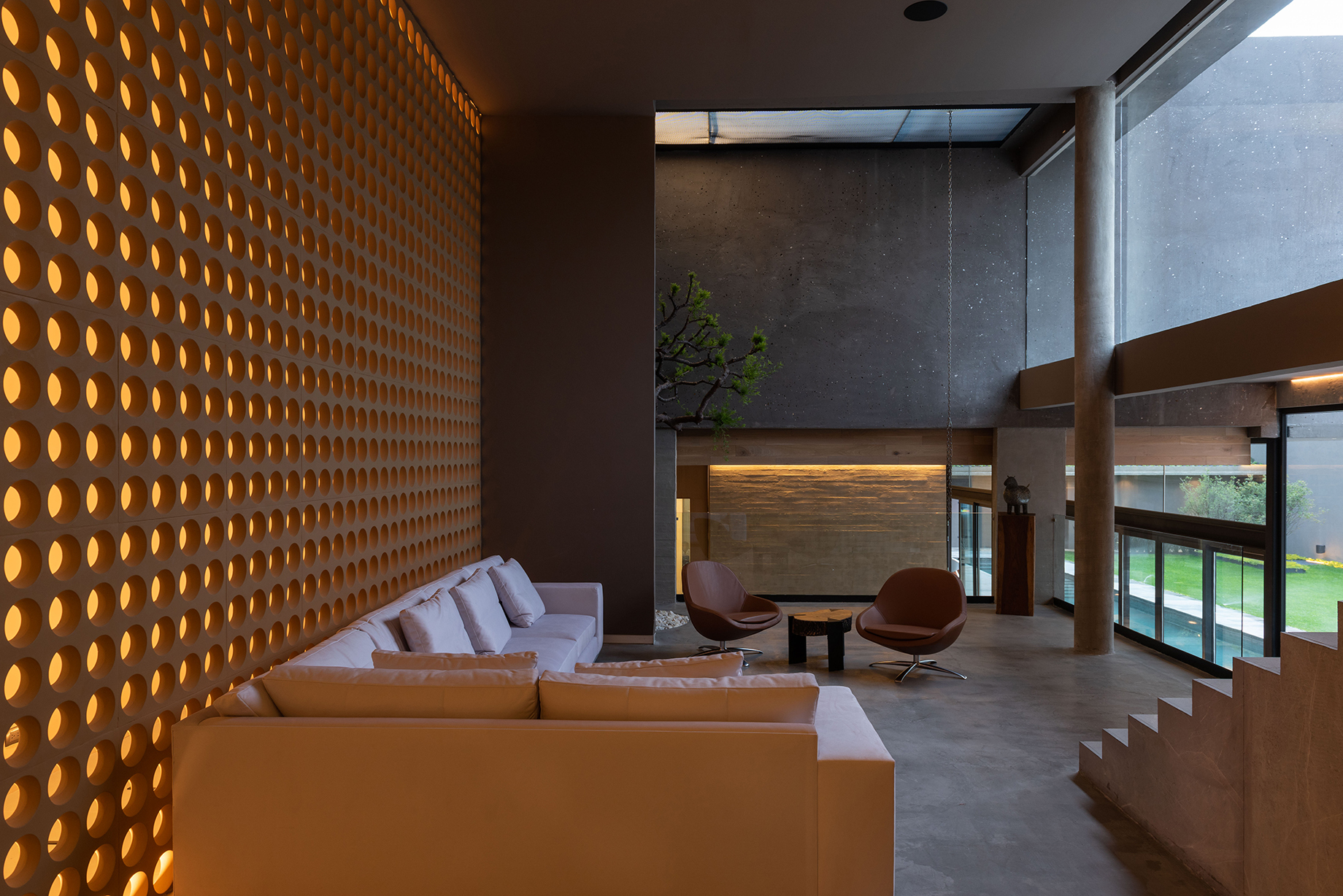 Living room with a perforated glowing screen wall, cream sofa and two leather chairs at dusk
