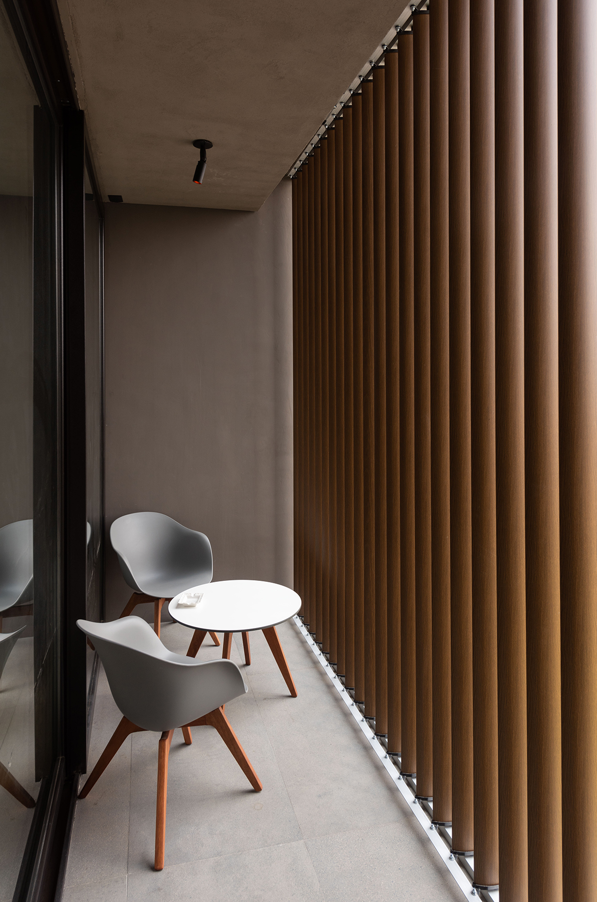 Narrow balcony with two grey chairs and a round white table beside floor-to-ceiling vertical timber louvers