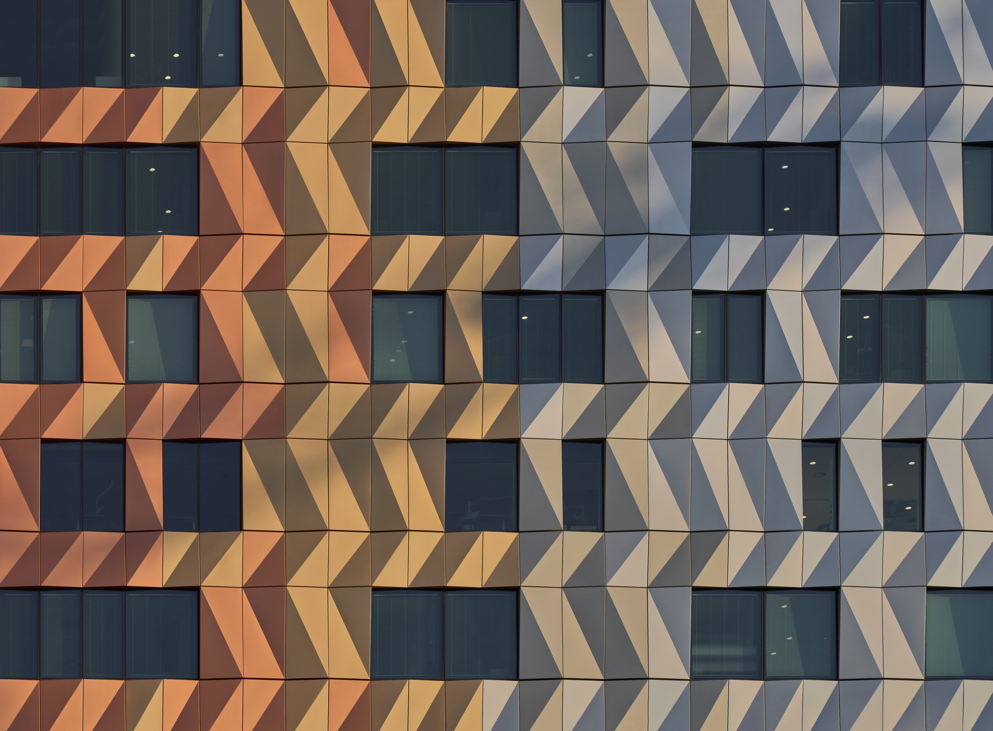 Facade detail of triangular metal panels creating a chevron pattern between horizontal window bands