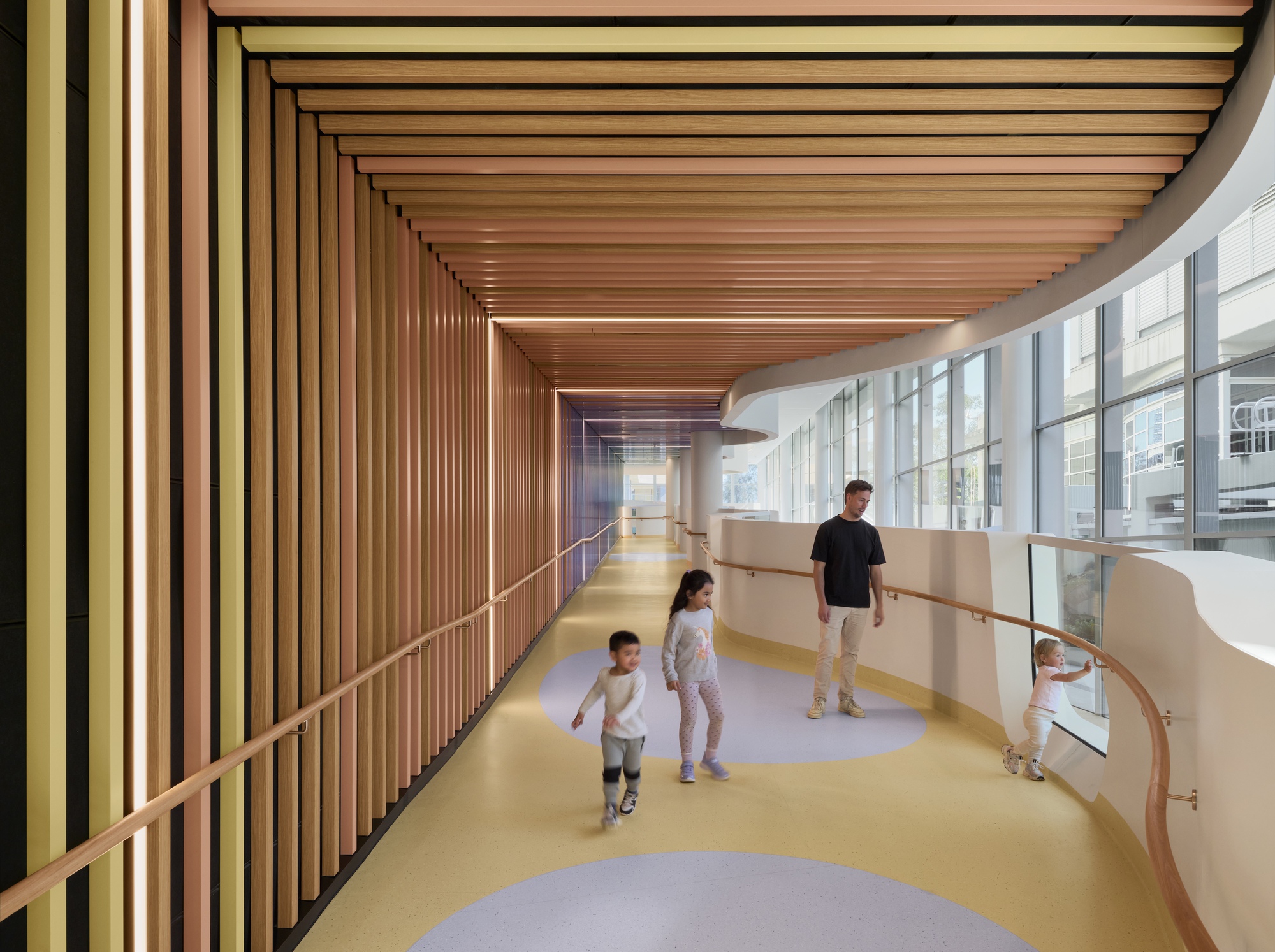 Curved corridor with timber slatted ceiling and yellow flooring as children walk beside glazed wall