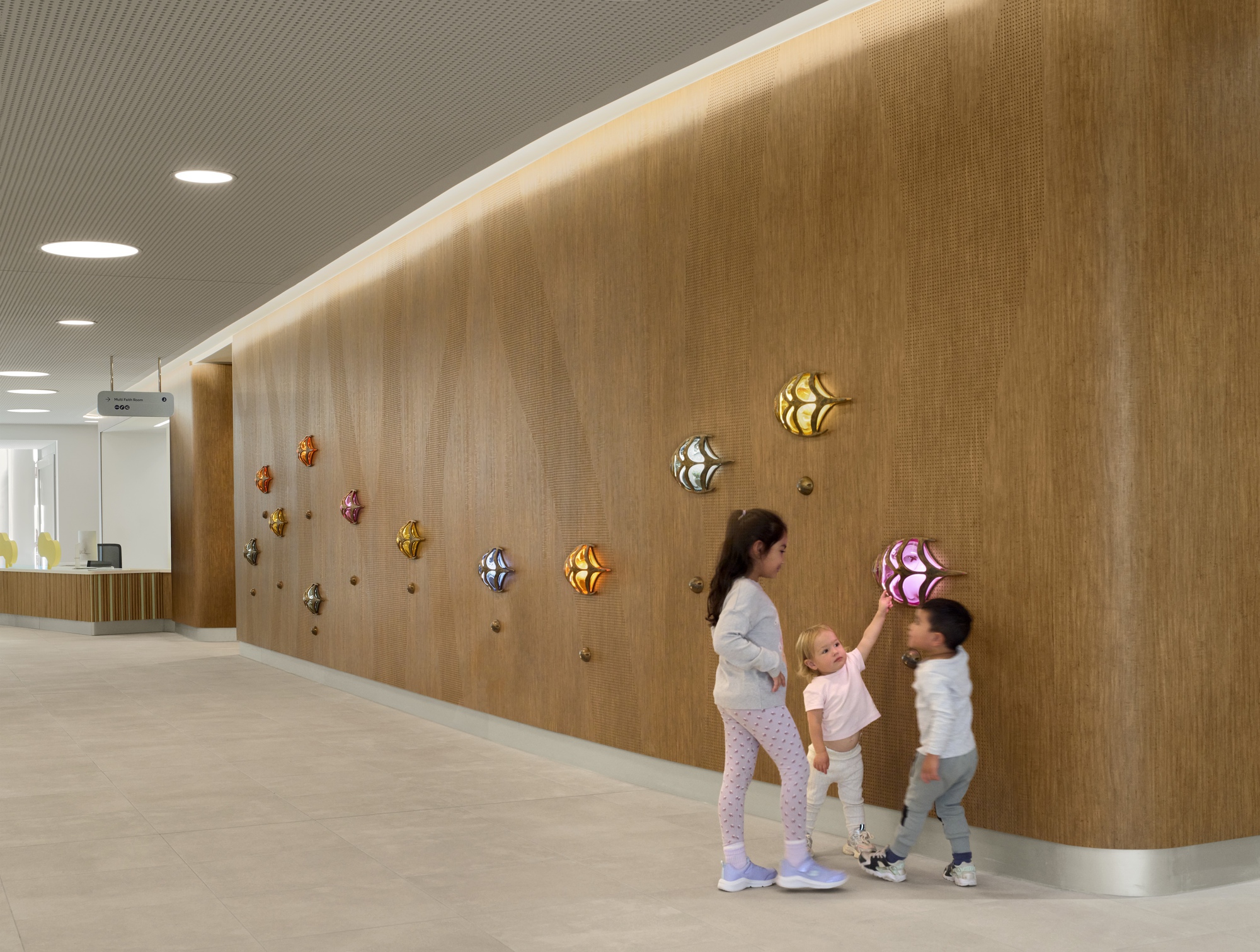 Curved timber wall with colorful wall-mounted lights and a woman with two children reaching toward them