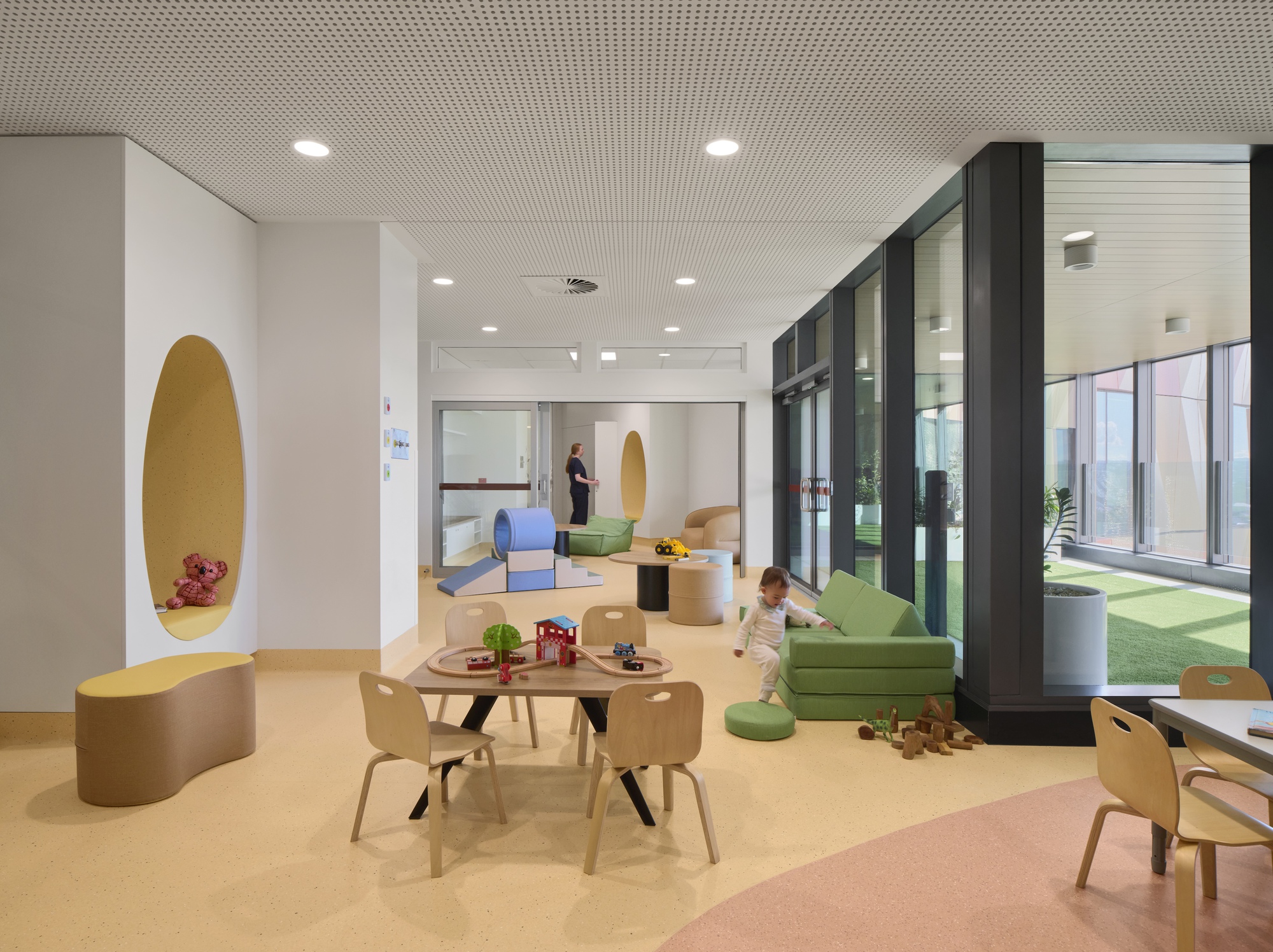 Play area with timber furniture, oval wall alcove, and glazed courtyard doors with a child on the floor