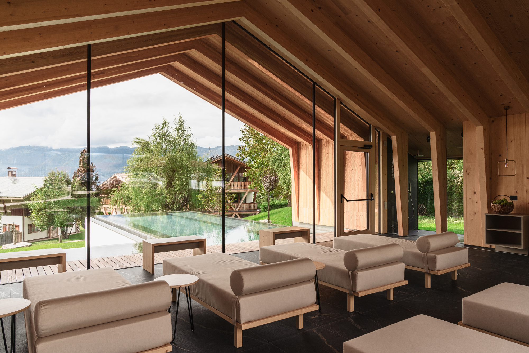 Interior lounge with exposed timber rafters and floor-to-ceiling glazing overlooking a pool and mountain landscape