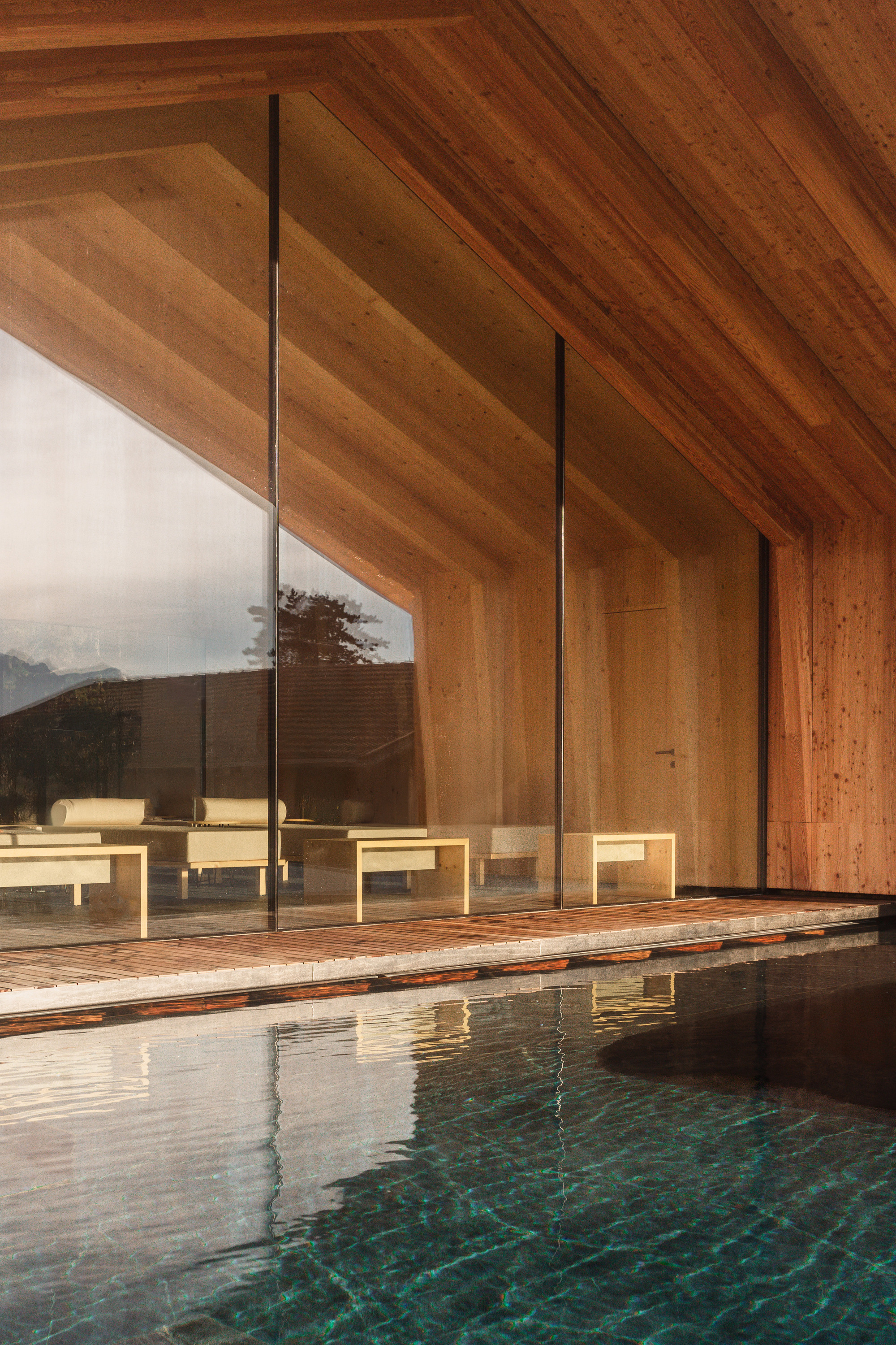 Pool edge with timber decking and glazed wall reflecting the gabled timber ceiling at dusk