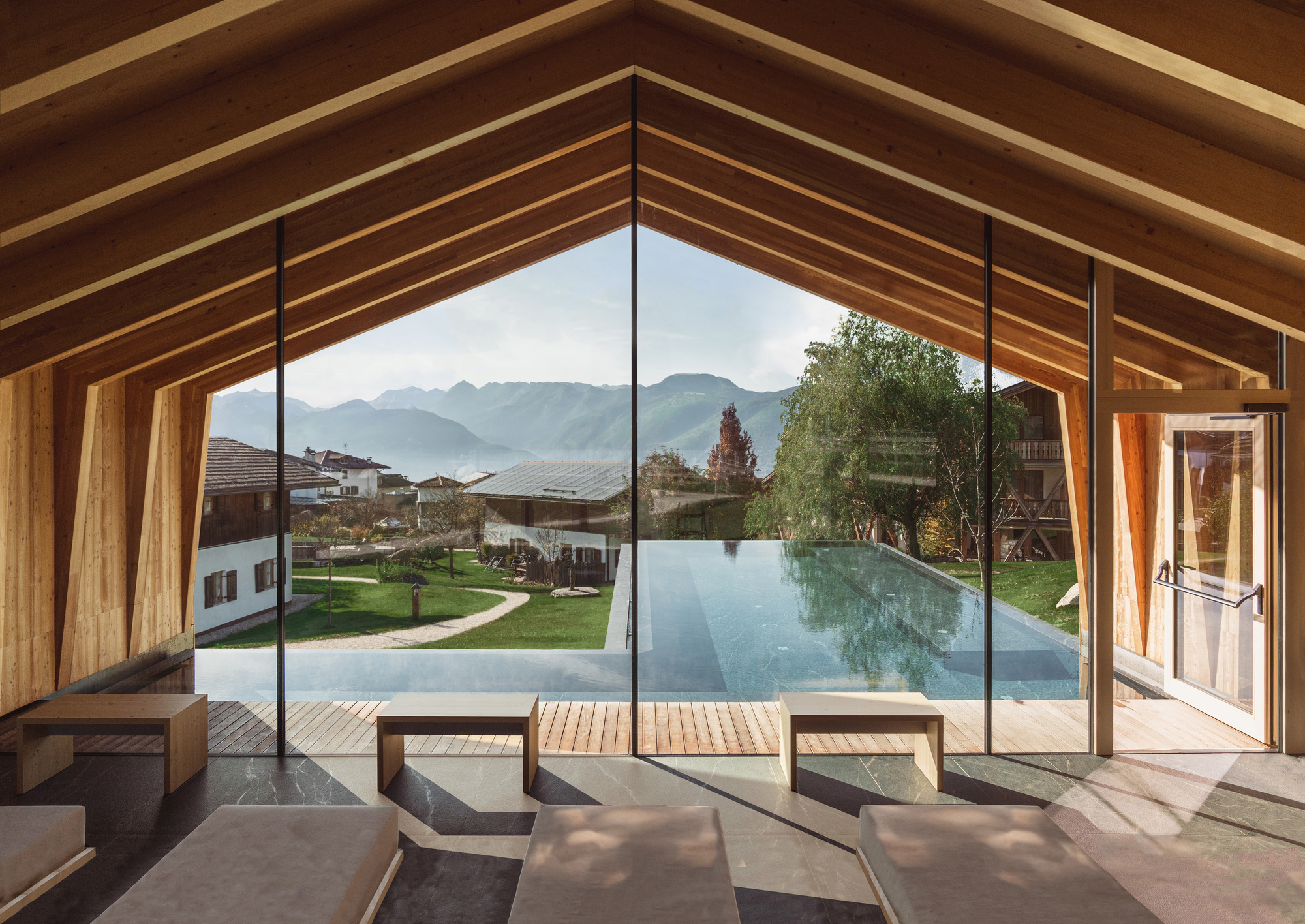 Interior lounge with exposed timber gabled ceiling and floor-to-ceiling glazing overlooking an infinity pool and mountains